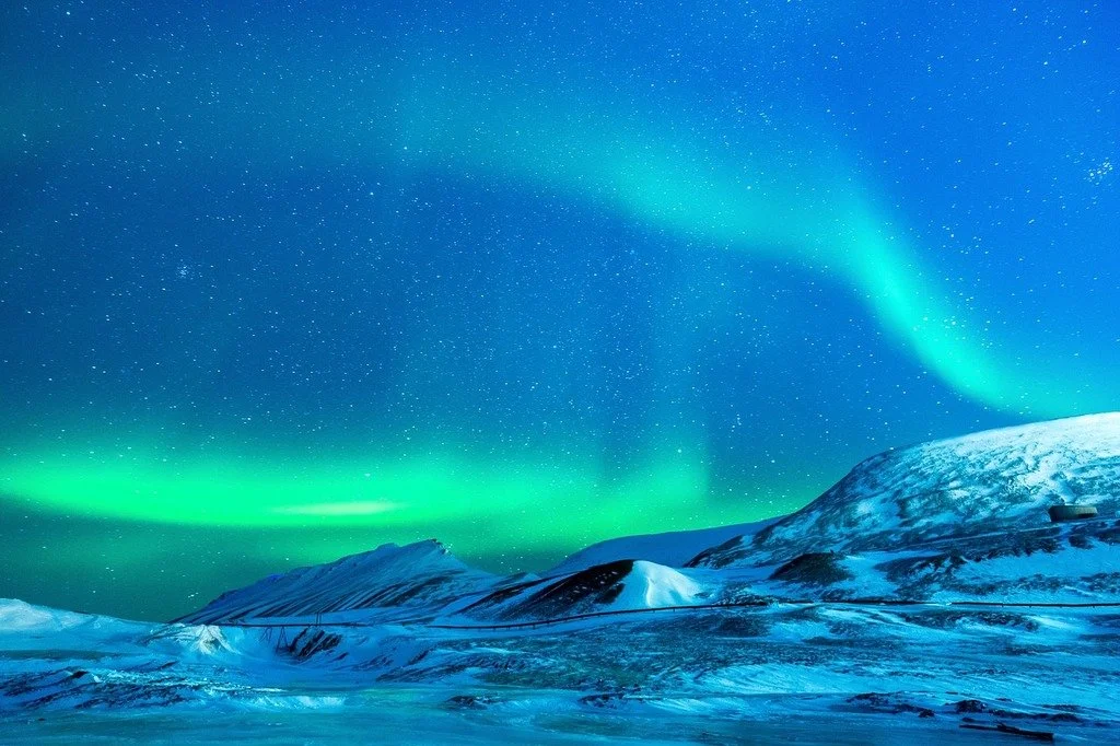 The greenish lights of the Aurora Borealis above the snowy mountains of Svalbard, Norway