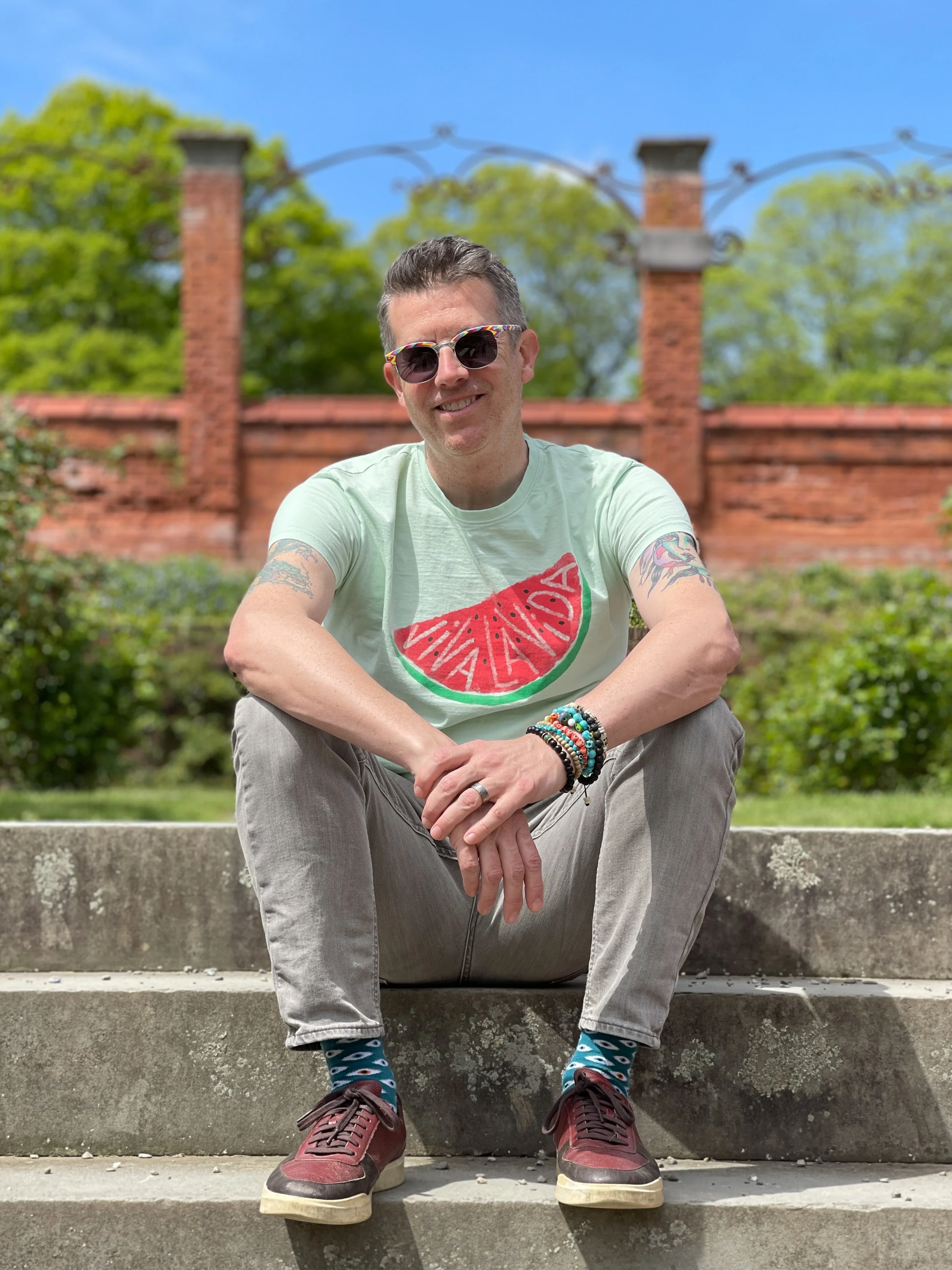 Man wearing sunglasses and watermelon T-shirt sits on steps at the Vanderbilt Mansion garden