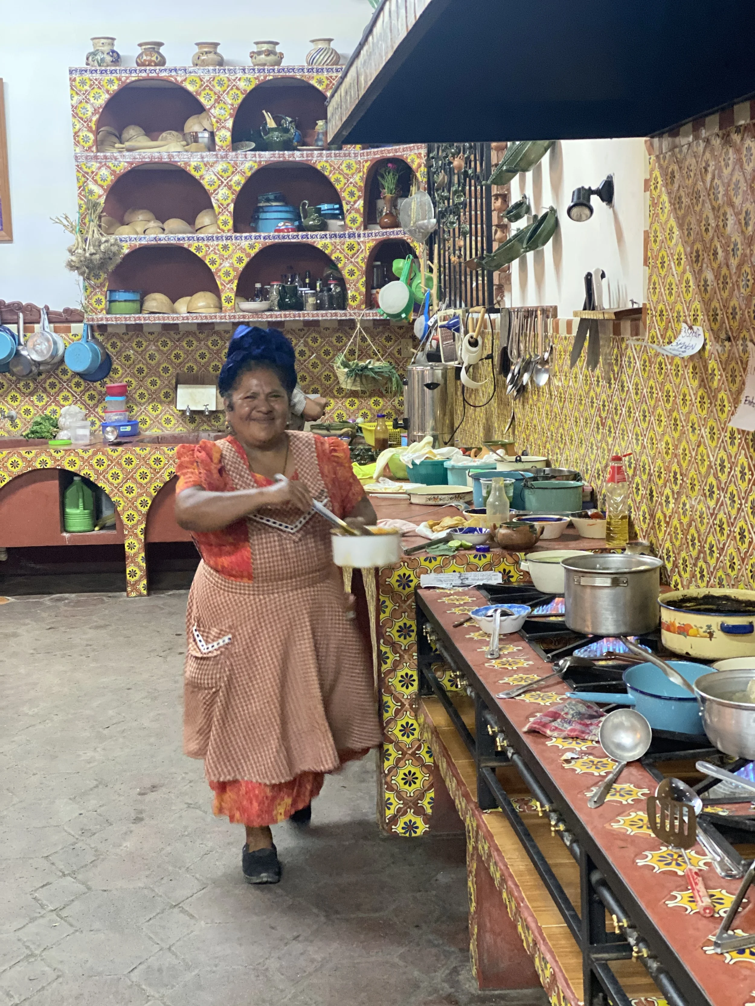 A smiling Abigail Mendoza Ruiz with a pan in her yellow tiled kitchen at Tlamanalli