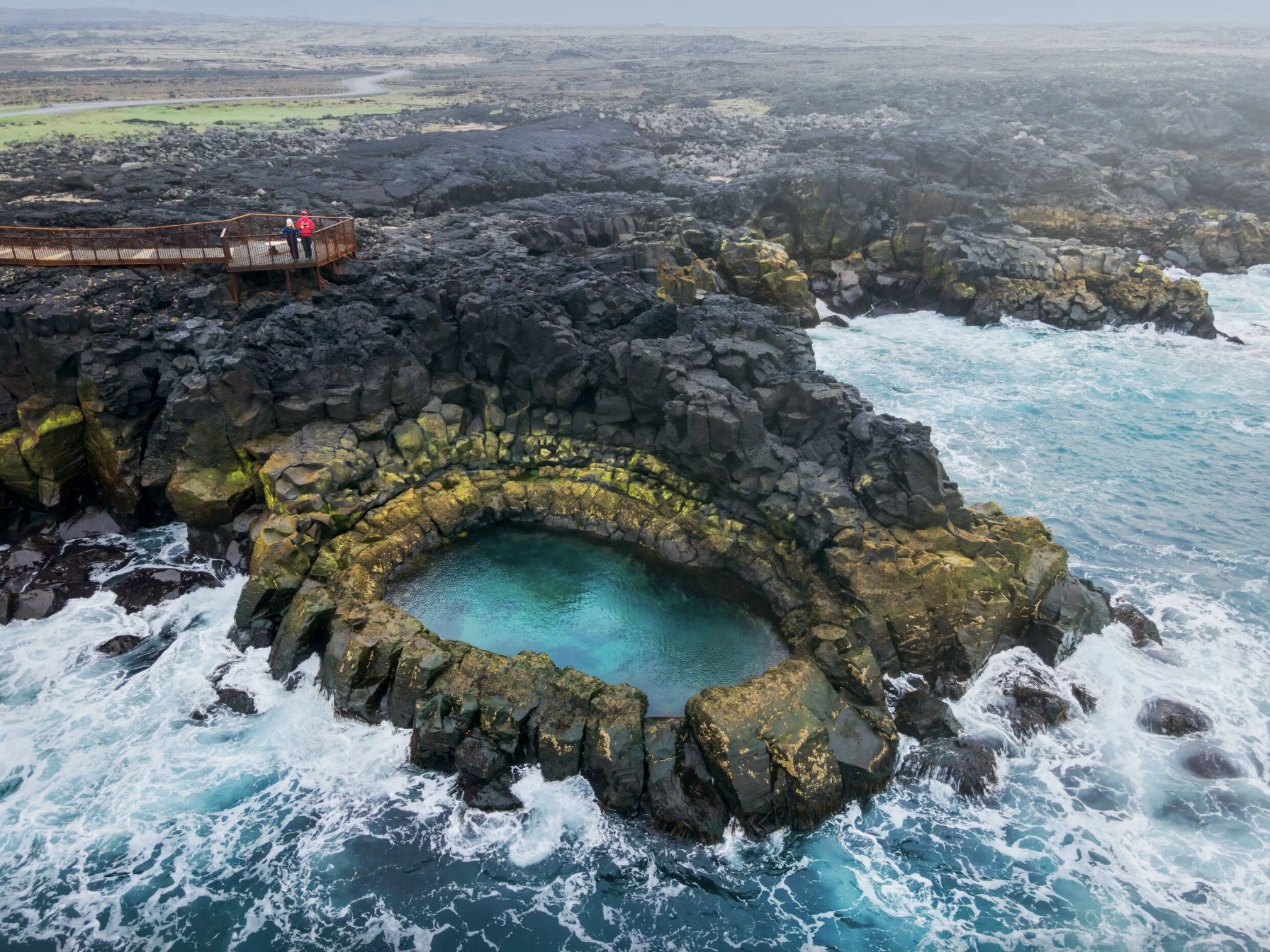 A round rock formation filled with water by a turbulent sea and overlook at Brimketill in Iceland