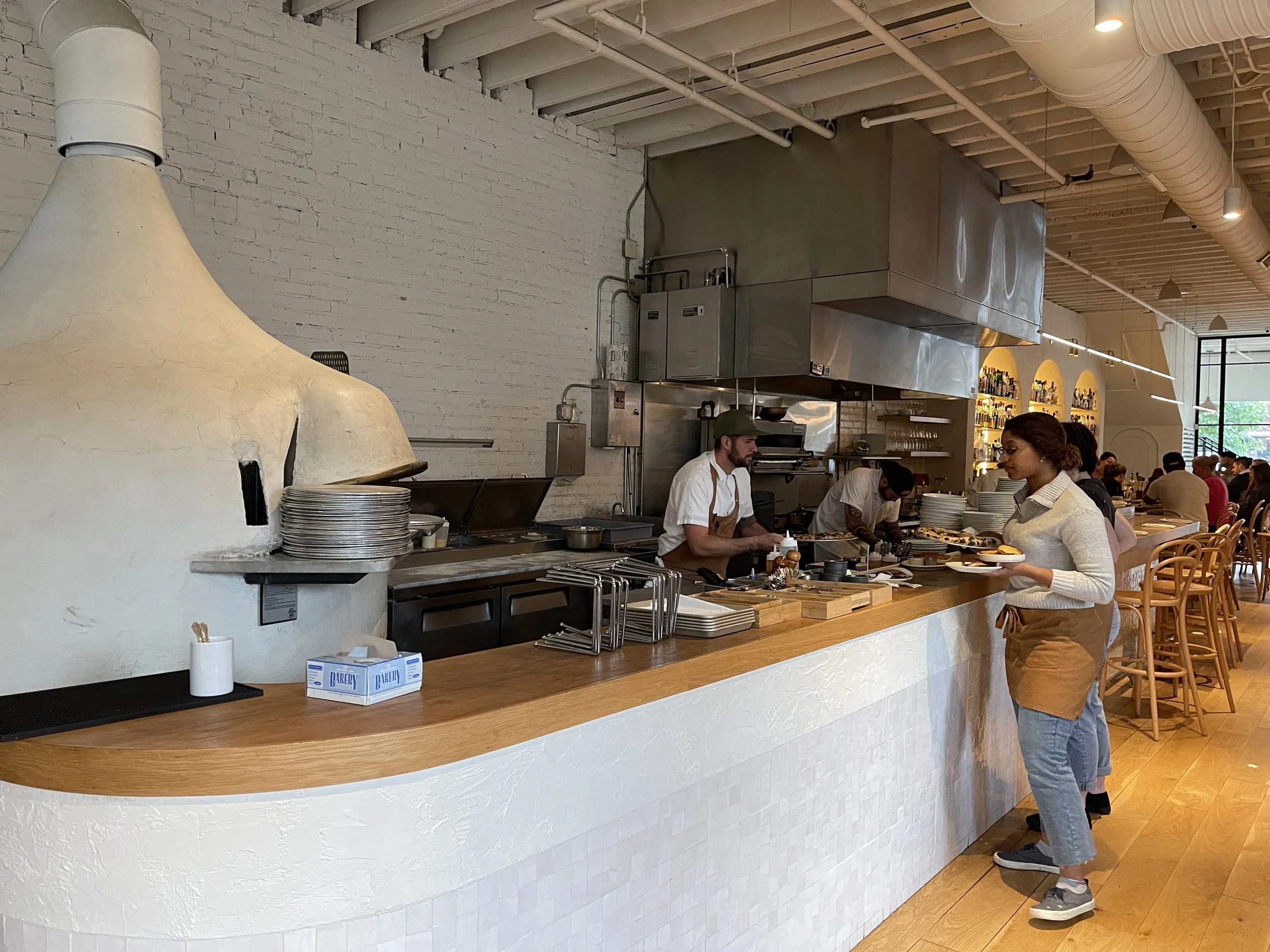 Wood-topped counter by white pizza oven, chef and server at West Rose in Ellicottville, New York
