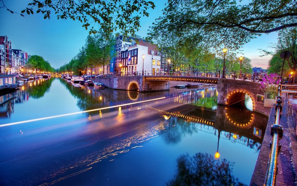 Amsterdam bridge lined with lights reflecting in the canal at twilight