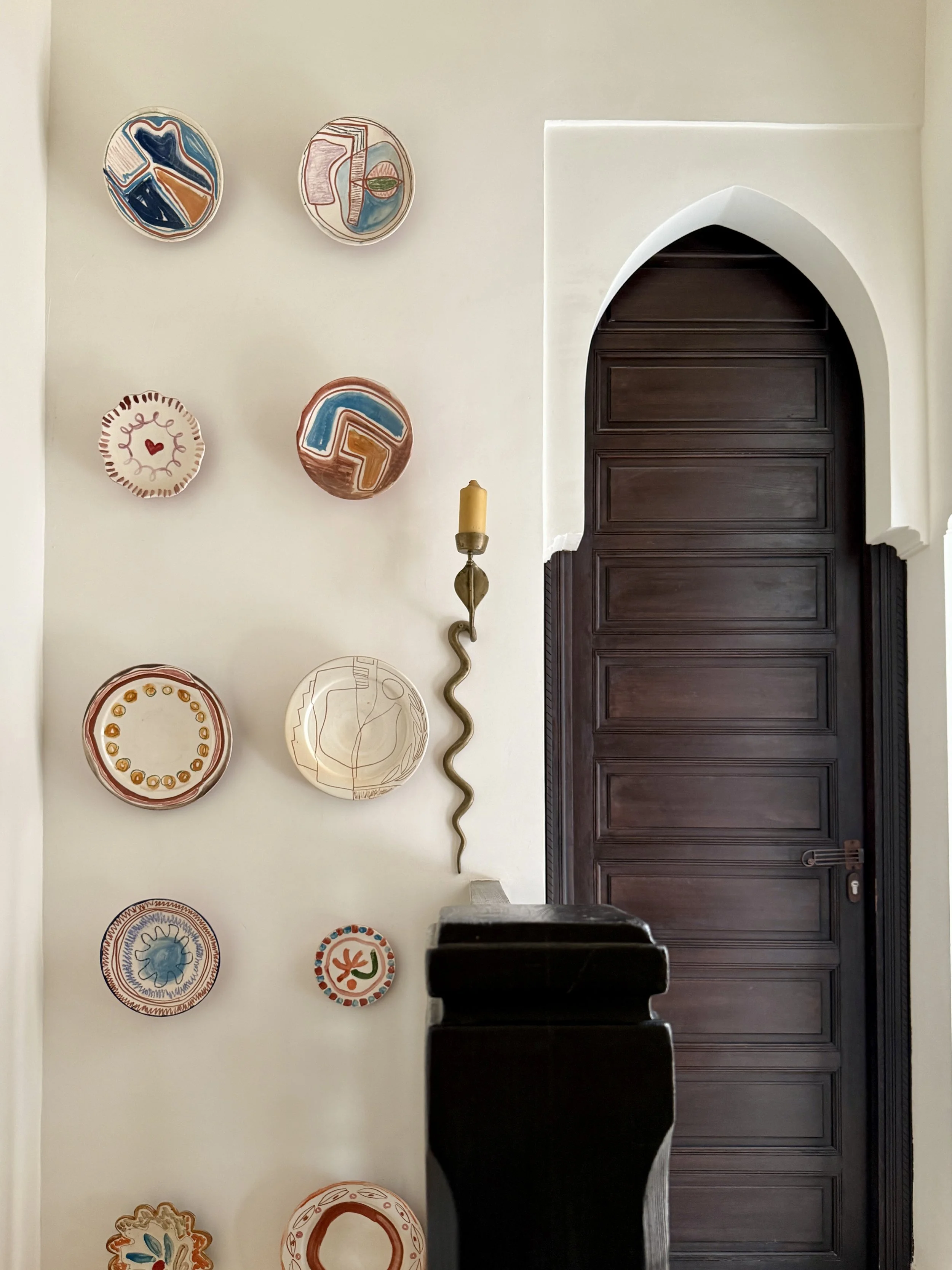 A gallery wall of hand-painted plates by LRNCE, accented by a vintage brass cobra sconce at Riad Rosemary in Marrkech
