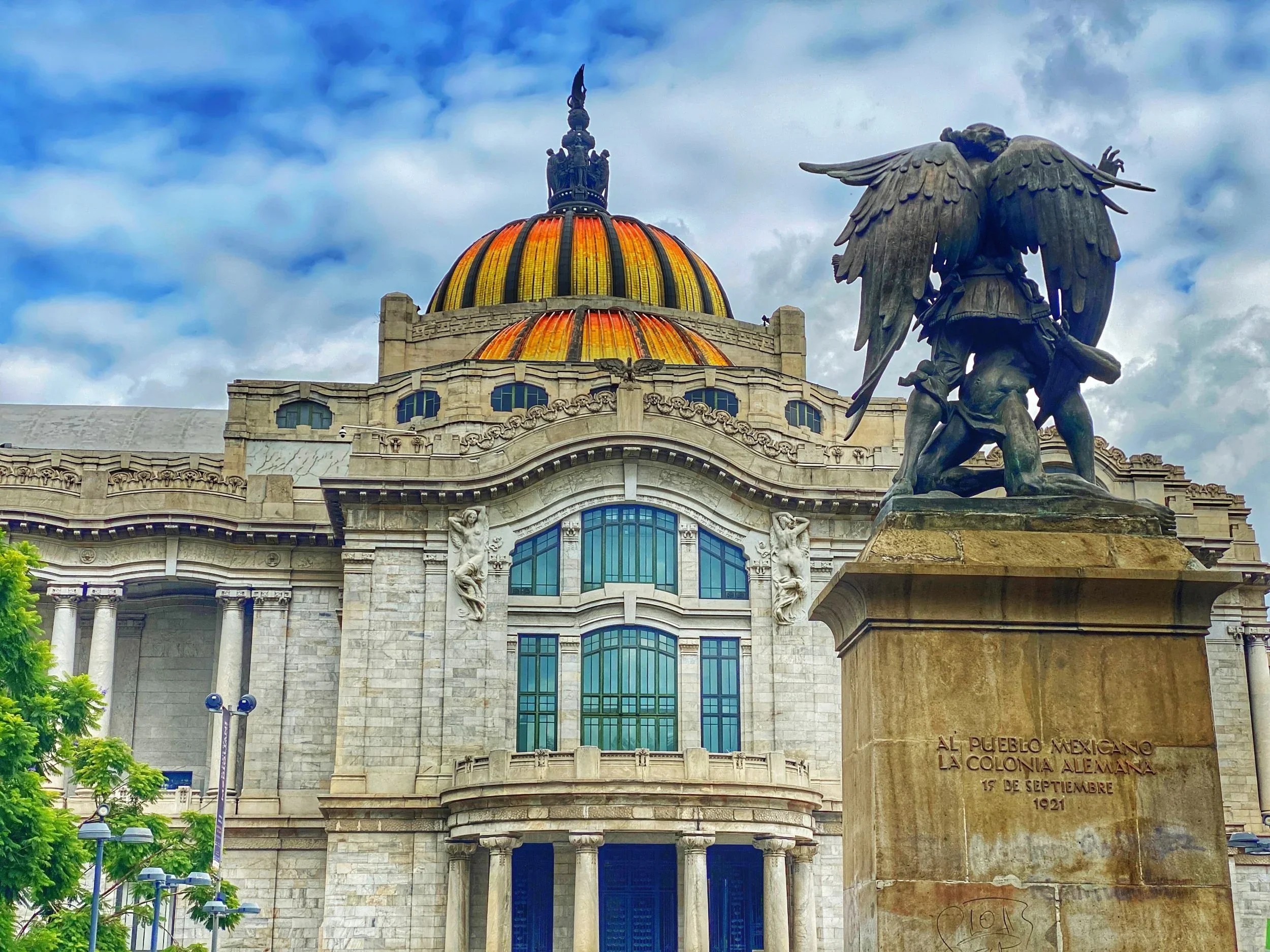 A statue in front of the orange and yellow domed Palacio de Bellas Artes in Mexico City's Centro neighborhood