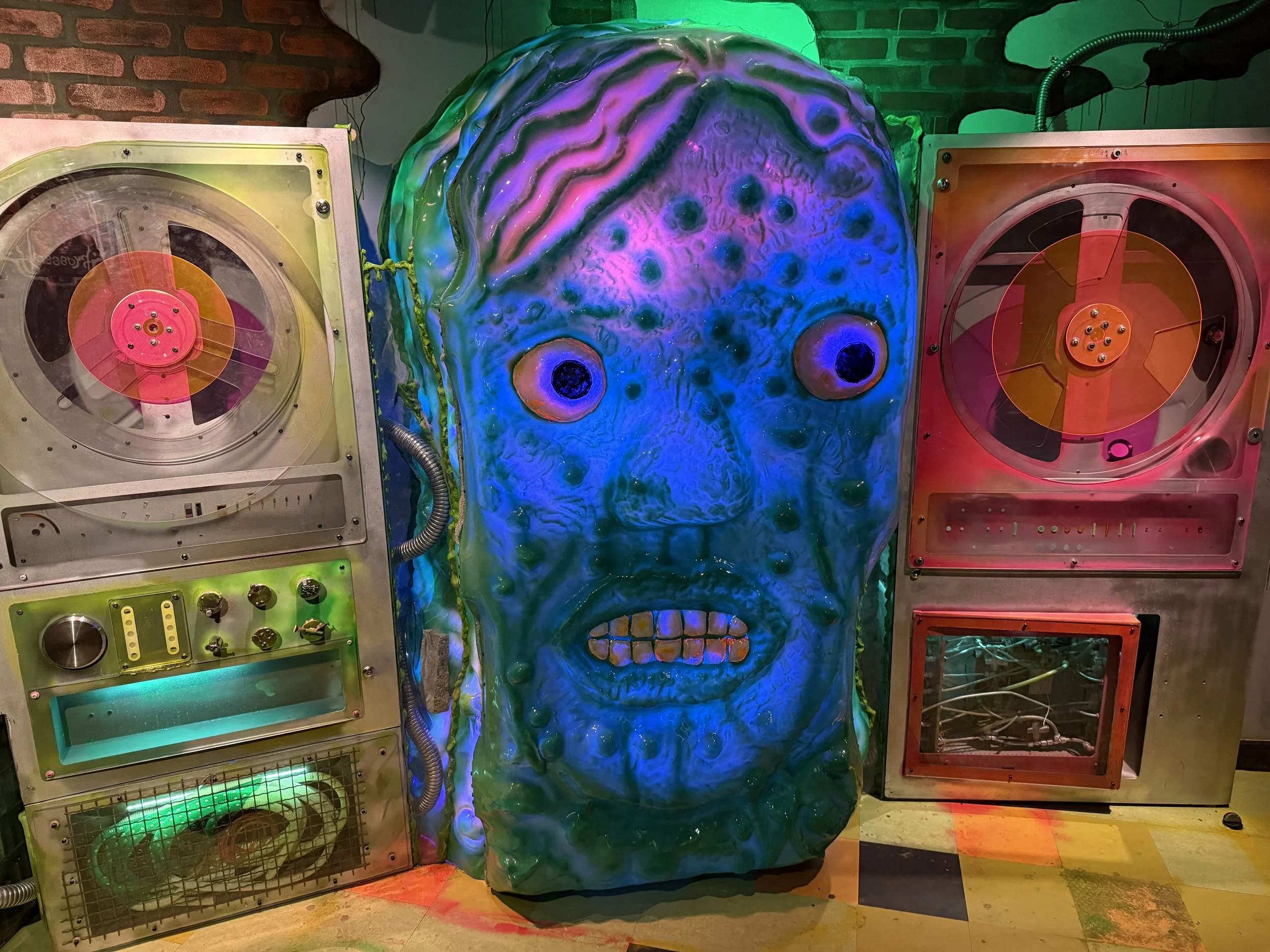 Retro audio equipment by a giant blue head at Meow Wolf Radio Tave in Houston, Texas