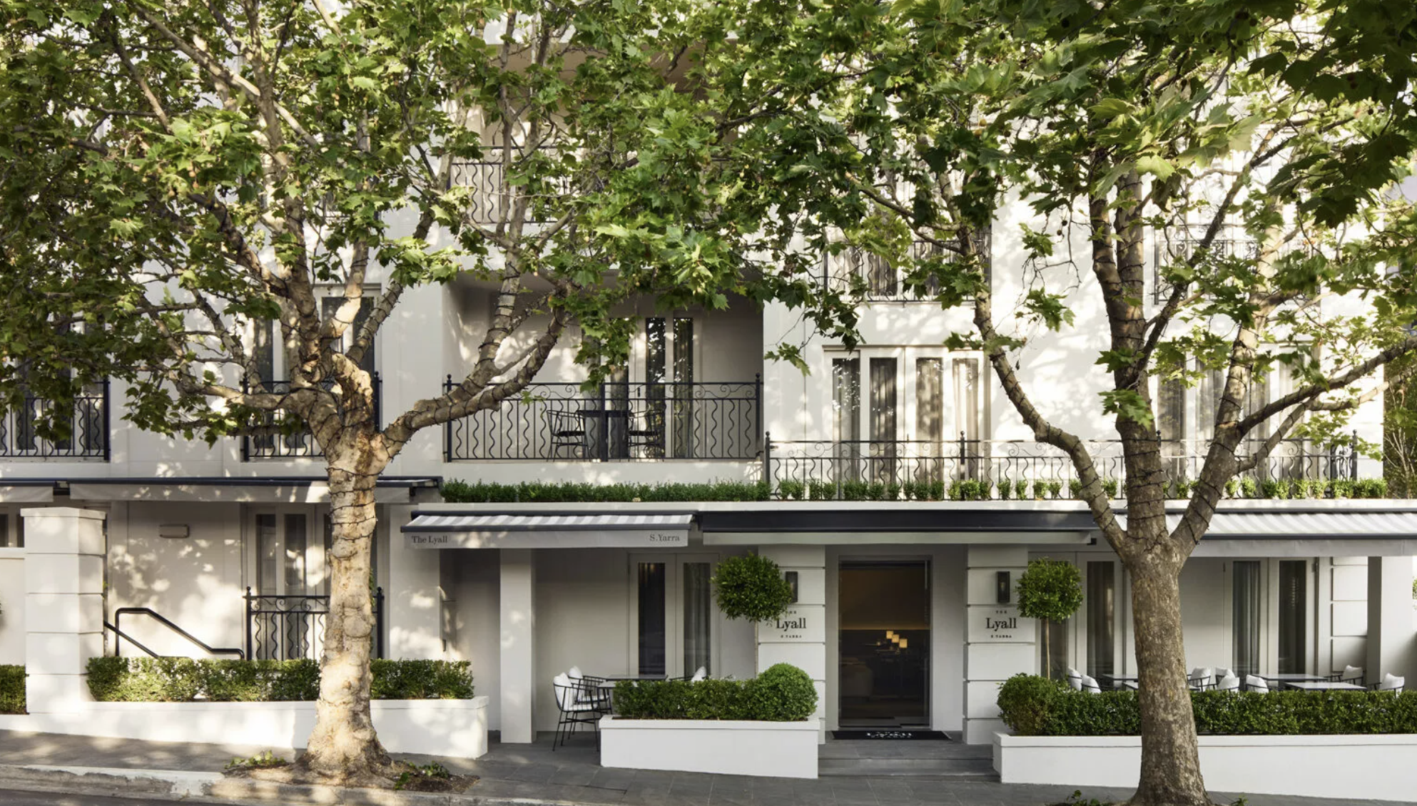 Two trees grow in front of the white facade of the Lyall hotel in Melbourne, Australia