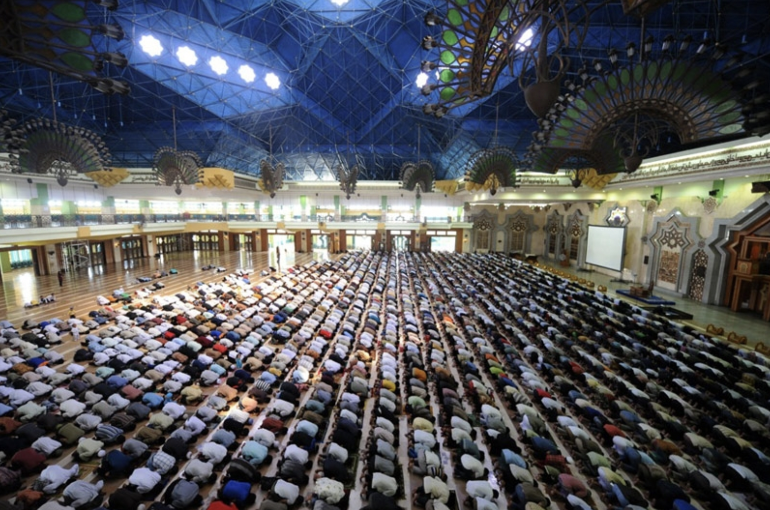 Huge group of Muslims kneeling and praying in mosque with blue ceiling