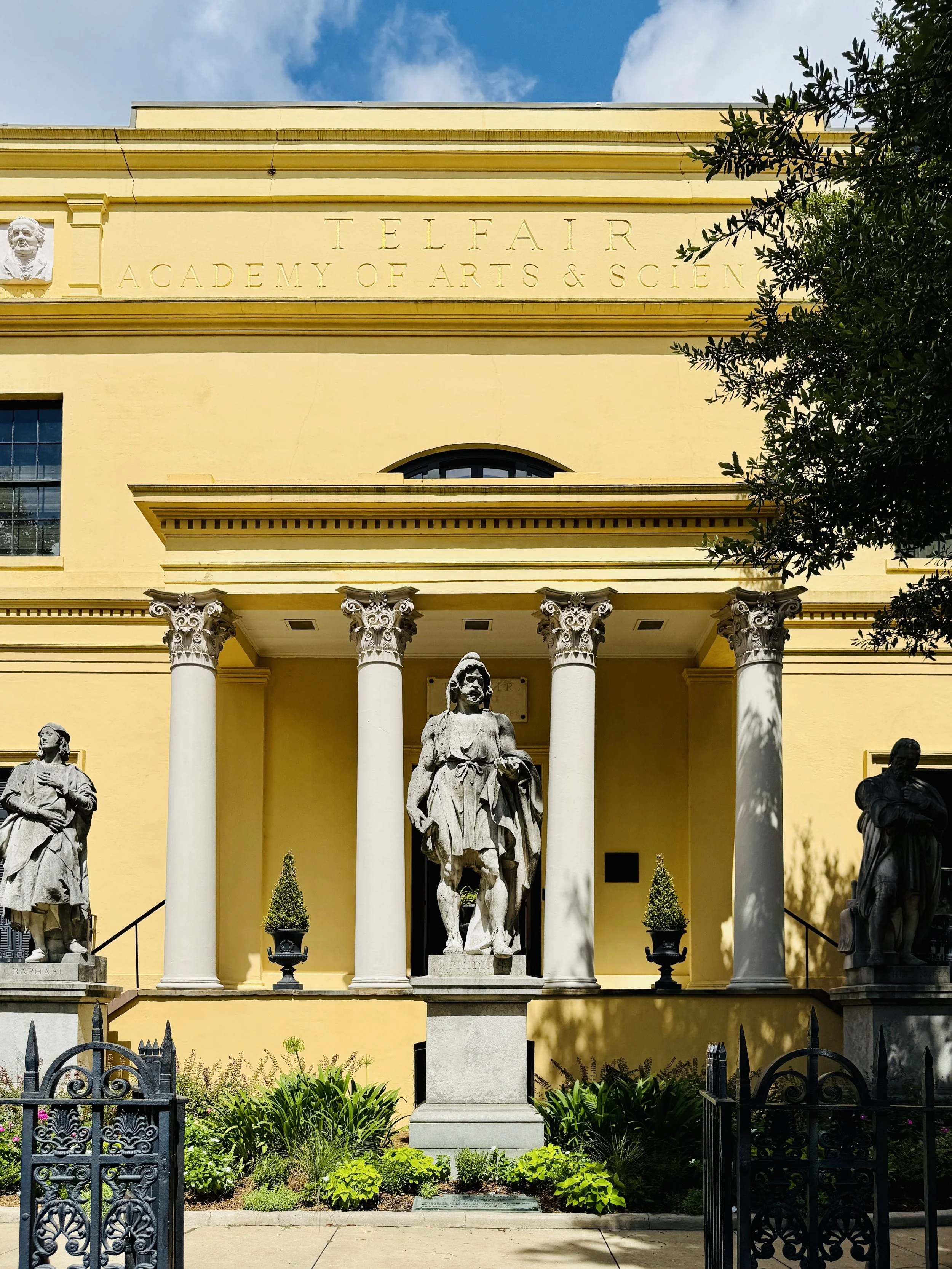 The yellow facade of the Telfair Academy in Savannah, Georgia, with statues of famous artists and classical columns