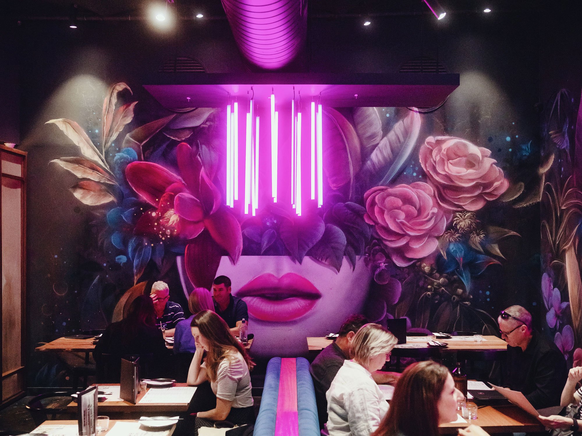 Pink neon lights hang from the ceiling by a cool mural with a woman's head filled with flowers at Hochi Mama in Melbourne, Australia