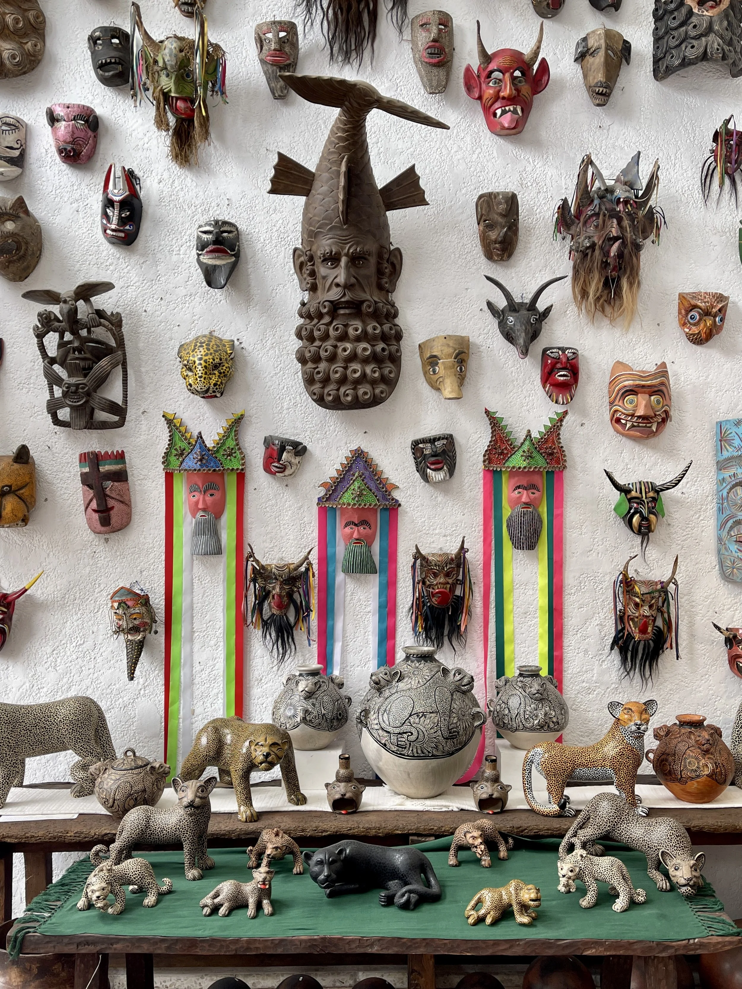 White wall covered with all sorts of wooden masks from Mexico, including bearded fishman, jaguars and devils