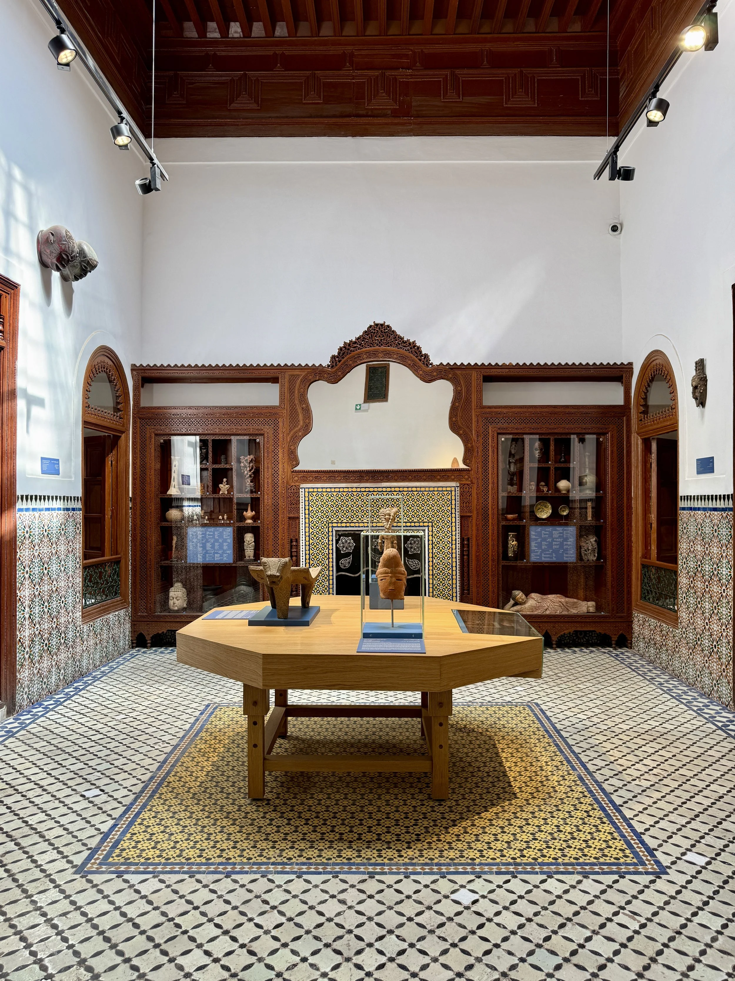 The room holding the Patti Birch collection at Dar el Bacha, Marrakech, Morocco, with an octagon-shaped table, wooden display cases and tiled floor and walls