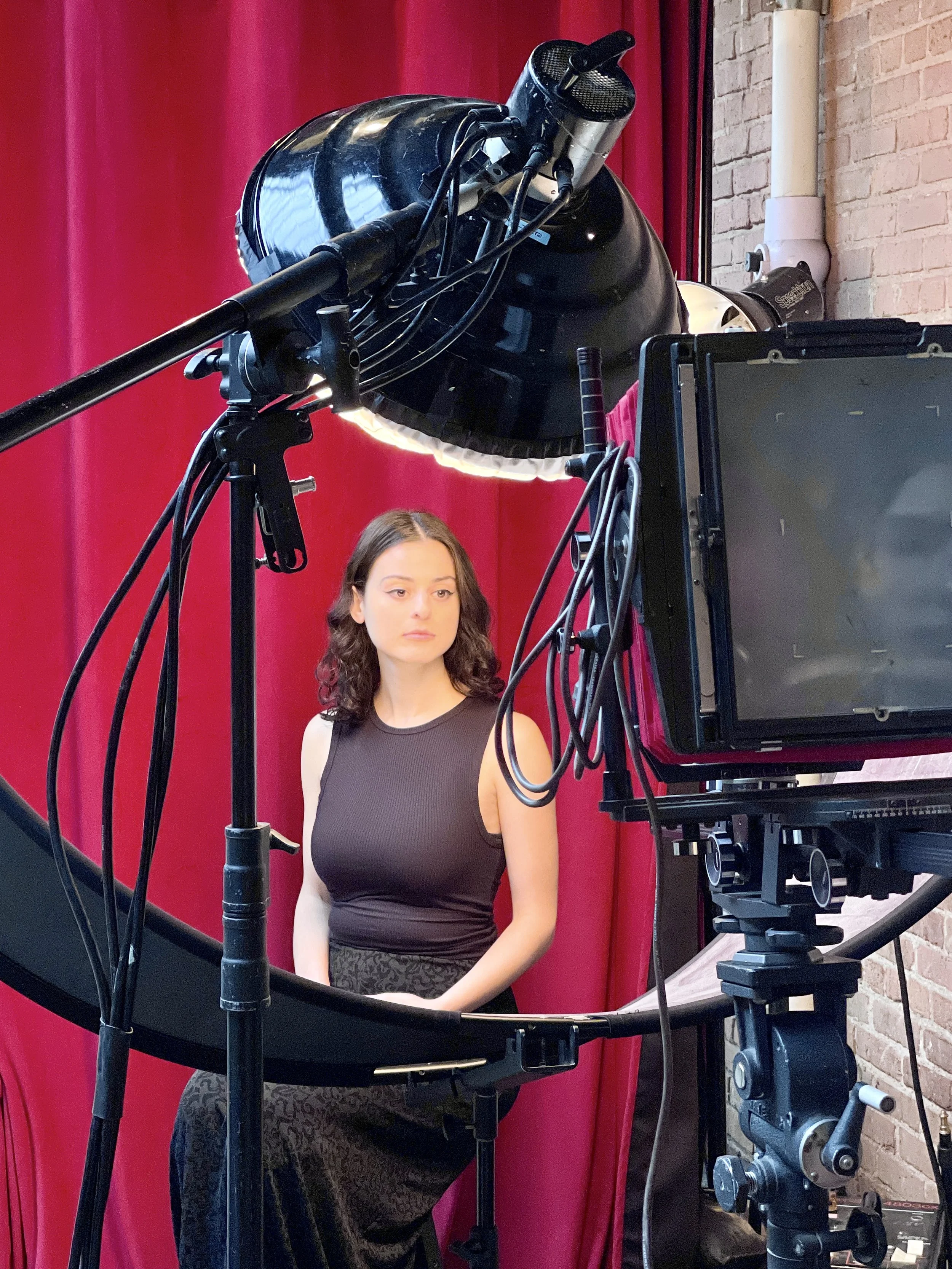 Young woman in black dress posing in front of large camera and light for Blkk Hand tintype photo