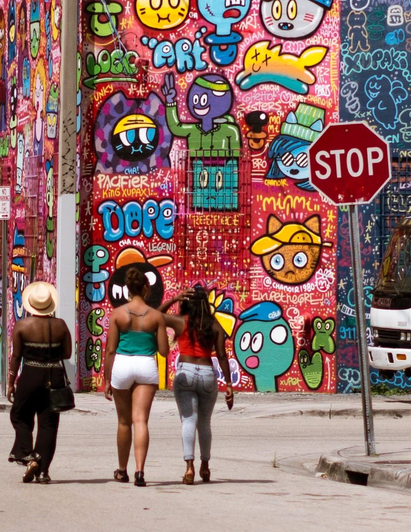 Three women walk past colorful murals in Wynwood in Miami, Florida