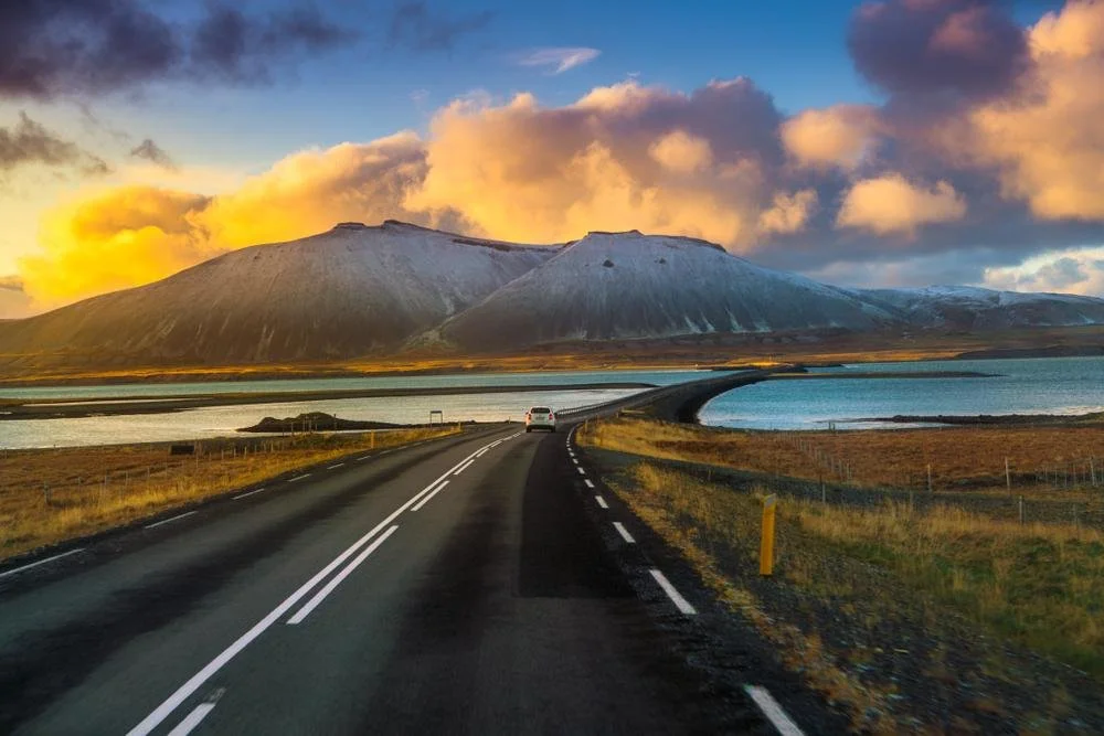 A car drives the Ring Road in Iceland, past mountains and water