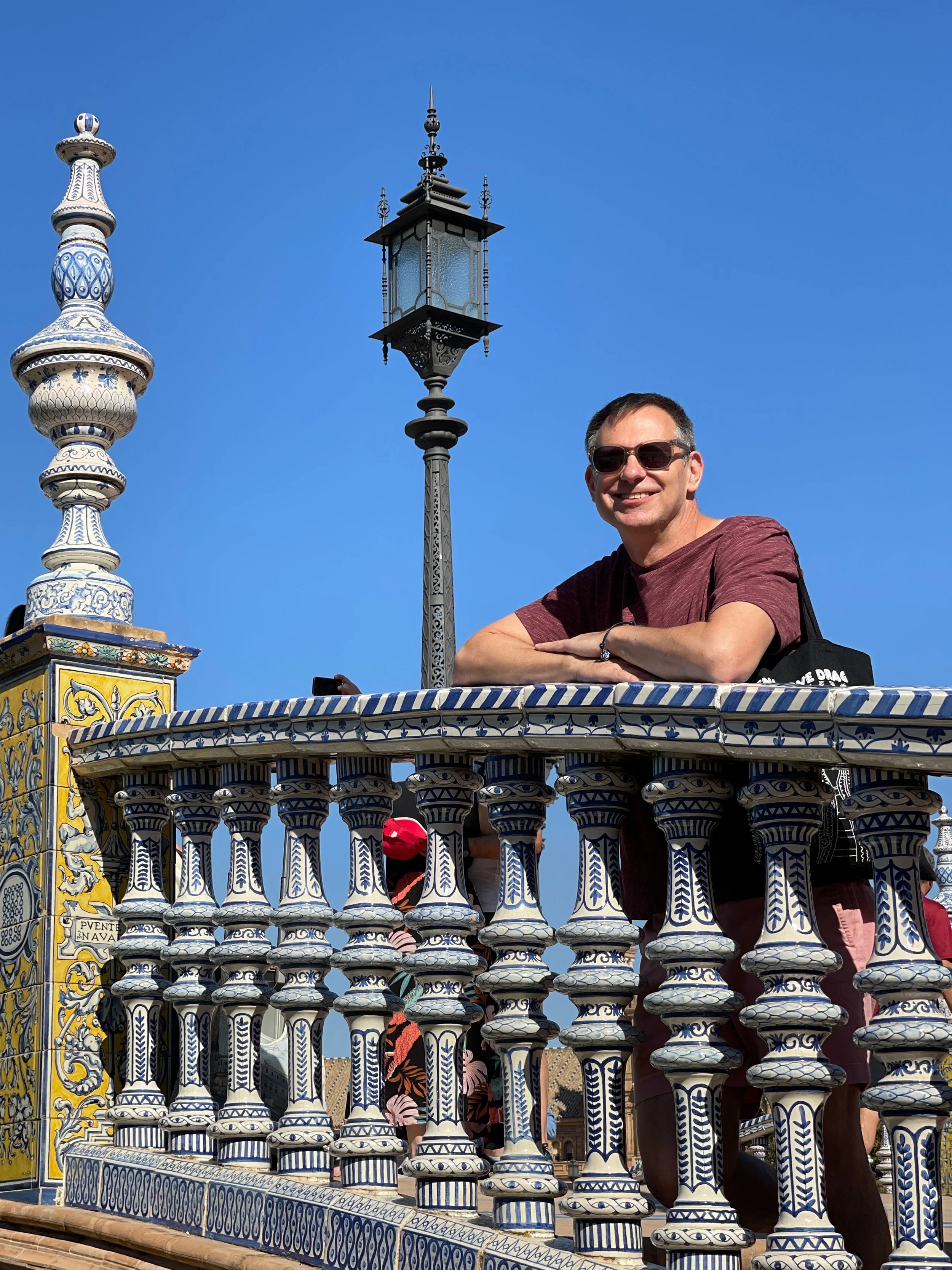 Man leans forward on blue and white bridge railing in the Plaza de España in Sevilla