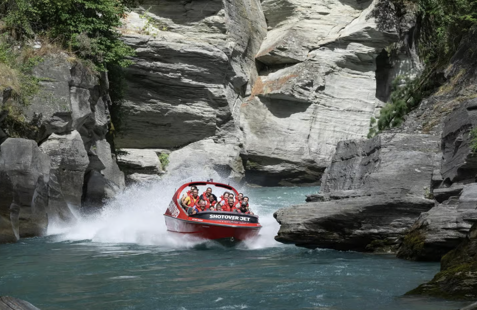 A red jet boat races down the Shotover River in Queenstown, New Zealand, past rock formations