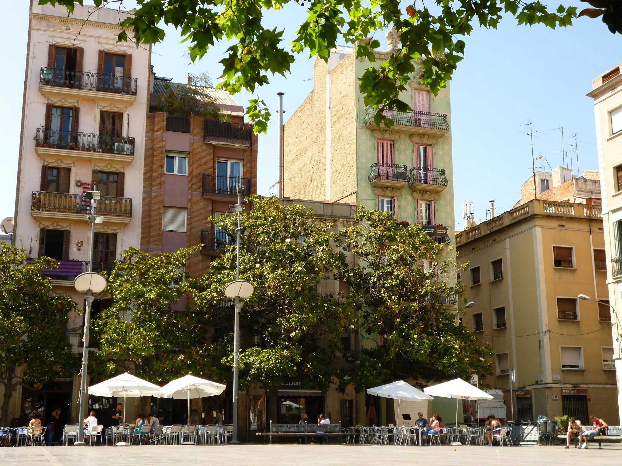 White umbrellas over tables and chairs in Plaça del Sol, with apartment buildings behind in Barcelona