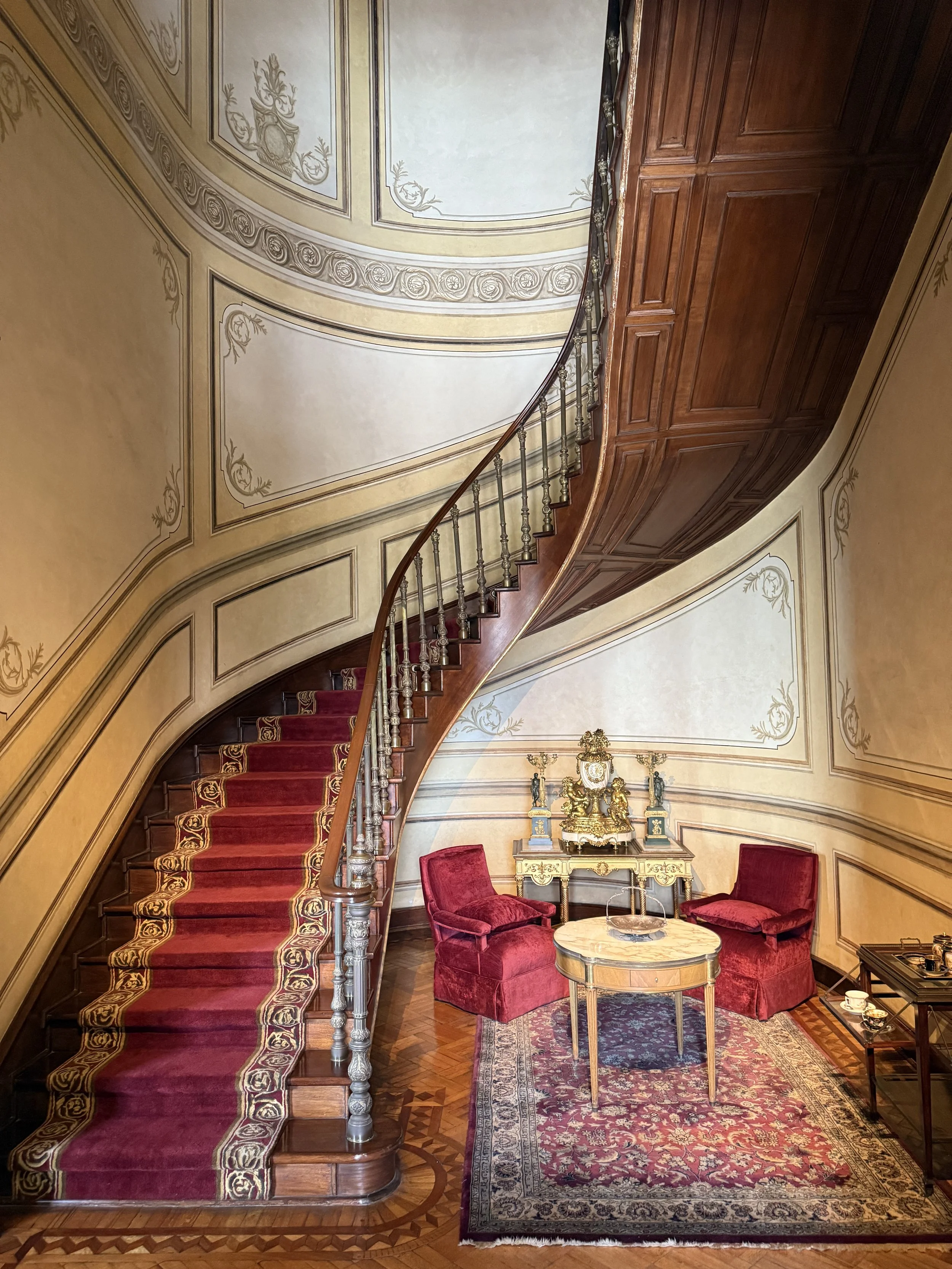 The curving Grand Staircase with red runner and a seating nook at Chapultepec Castle