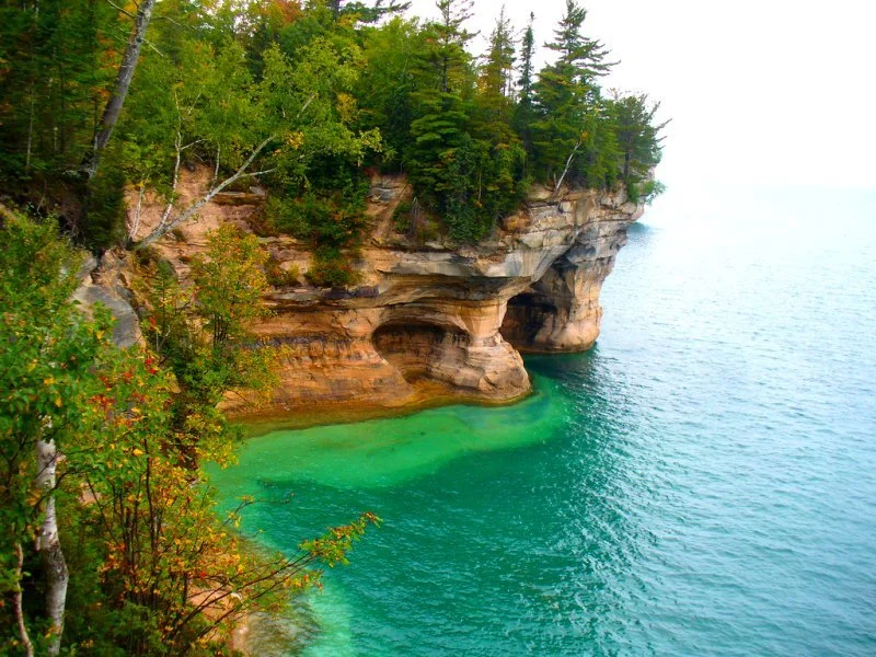 Waterside cliffs with caves and trees above the greenish waters of Lake Superior