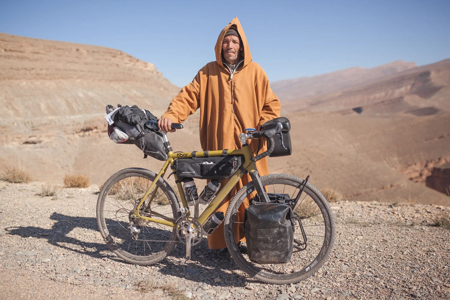 A Berber man holds a bike loaded with packs by the Atlas Mountains in Morocco