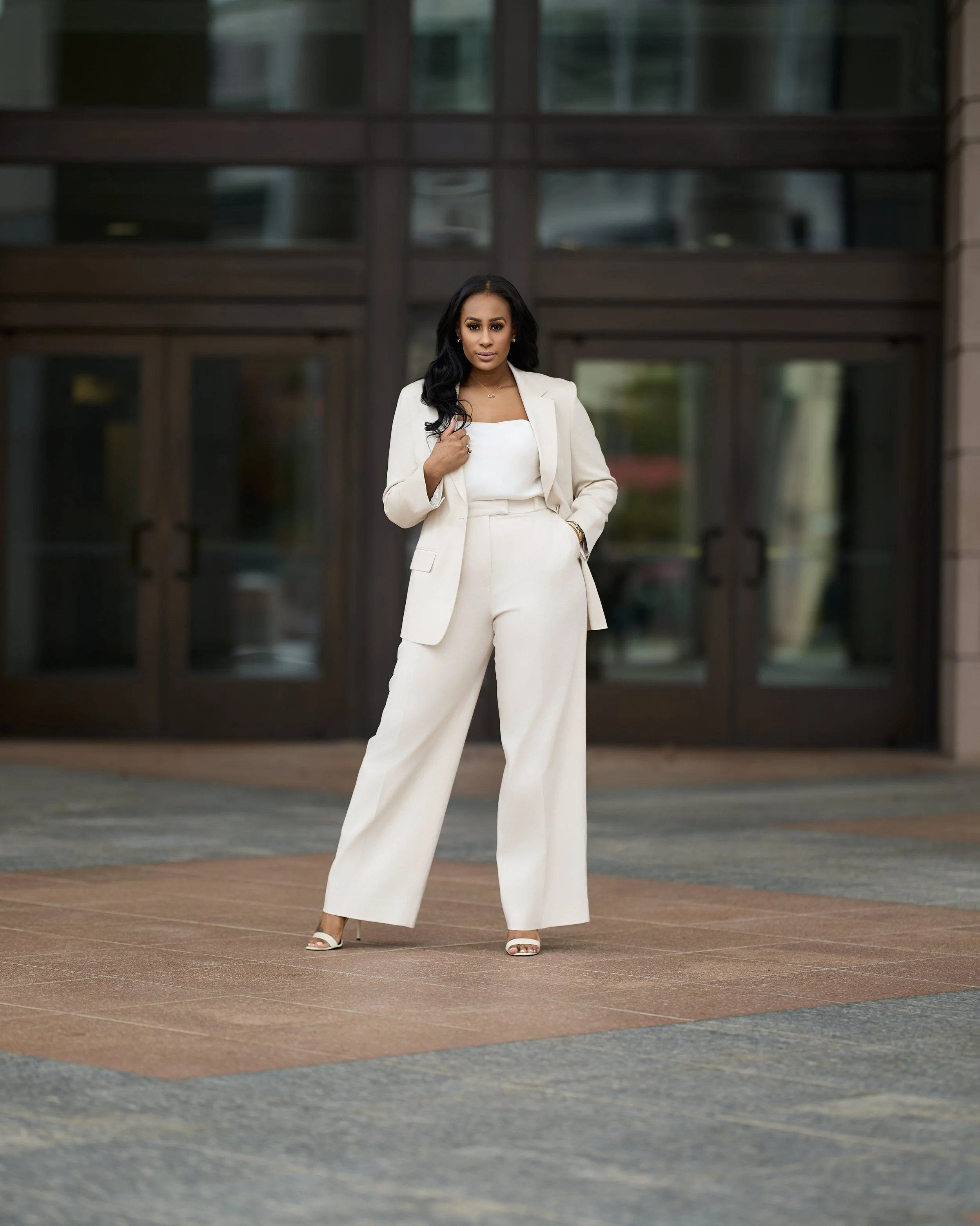 A woman in a white suit standing in front of a building with glass doors.