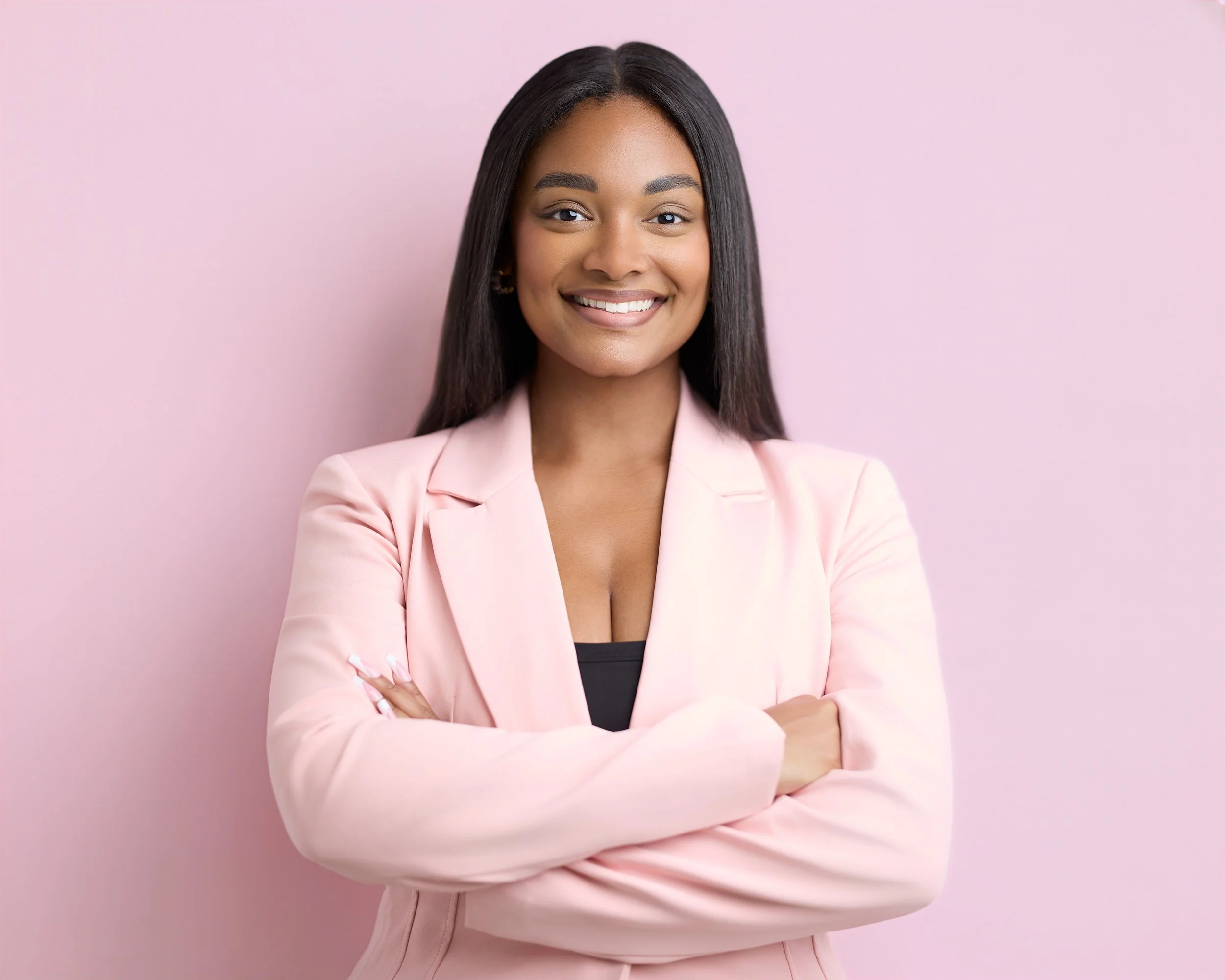 A woman with long straight black hair smiling and wearing a light pink blazer over a black top, standing against a pink background.