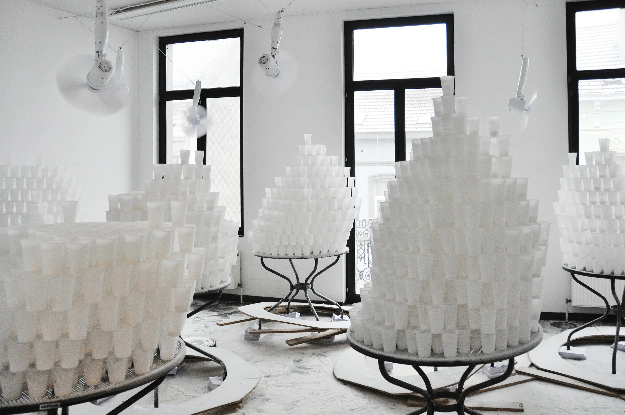 Parallax View, 2017, Garden tables, plastic cups, wood, ventilators, cleaning robots and salt. Installation view at Morpho, Brussels. Photo by: Kiki Petratou