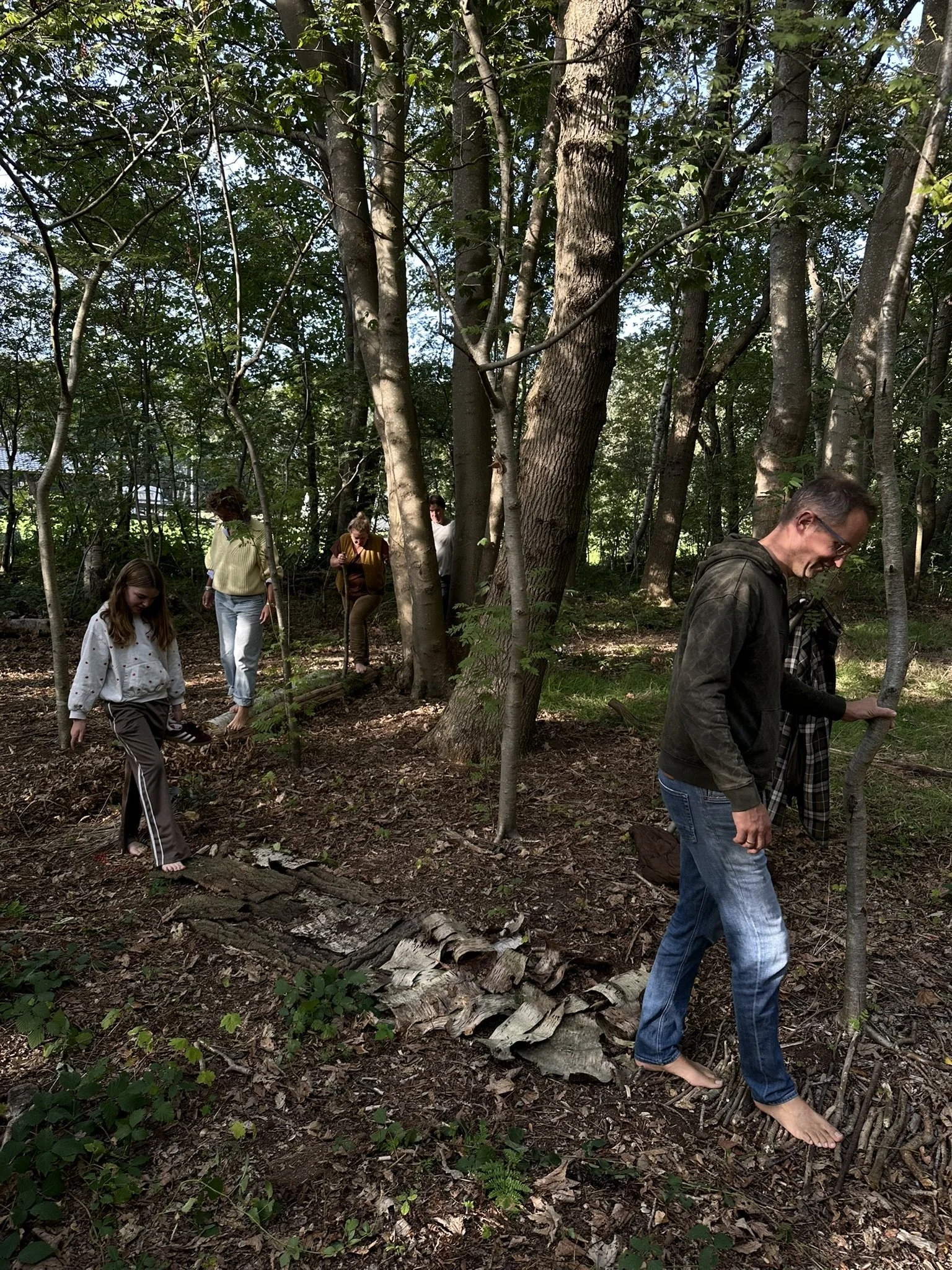 Mensen wandelen en staan in een bos, met bomen en takken rondom.