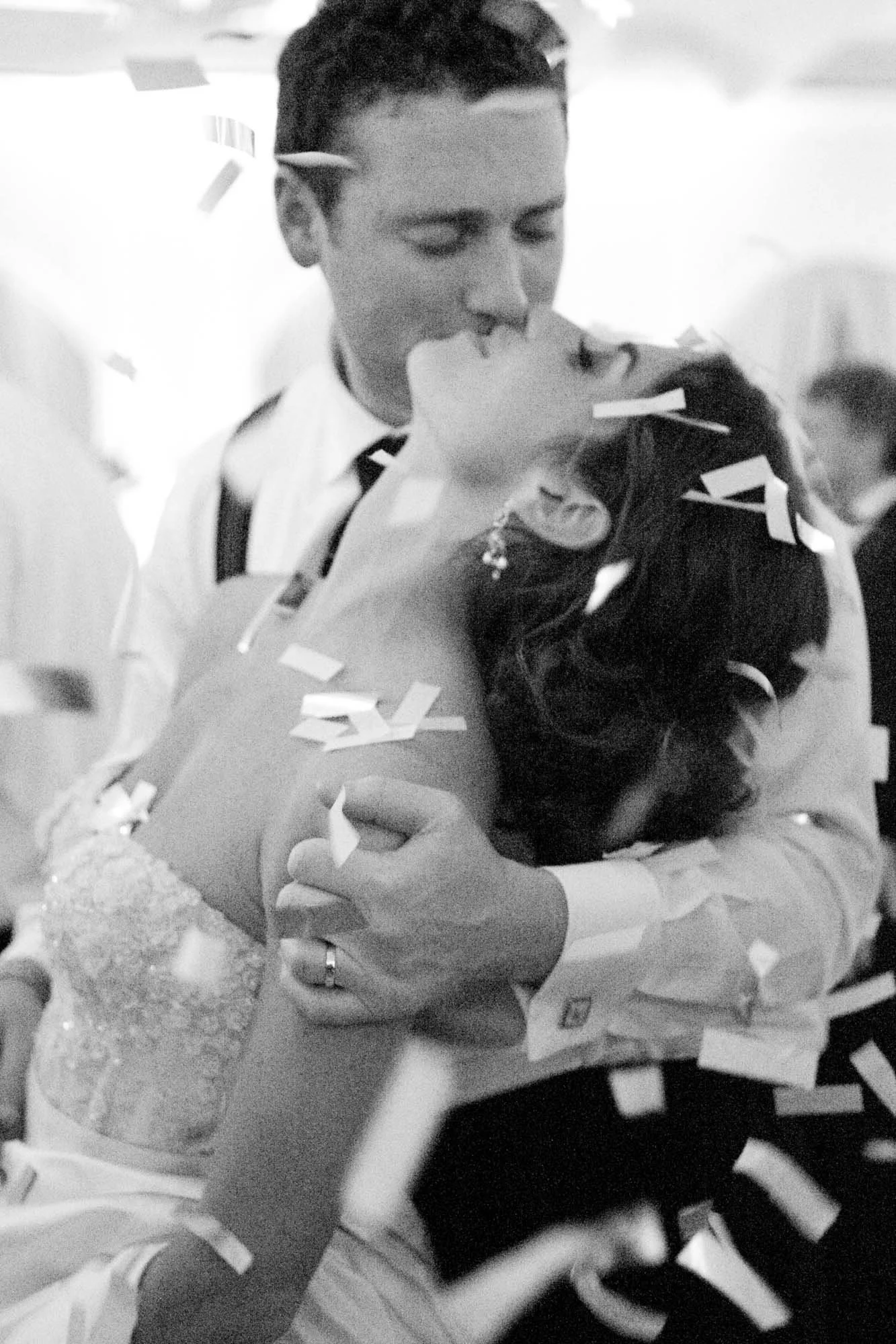 A couple dancing closely at a celebration, surrounded by falling confetti in black and white.