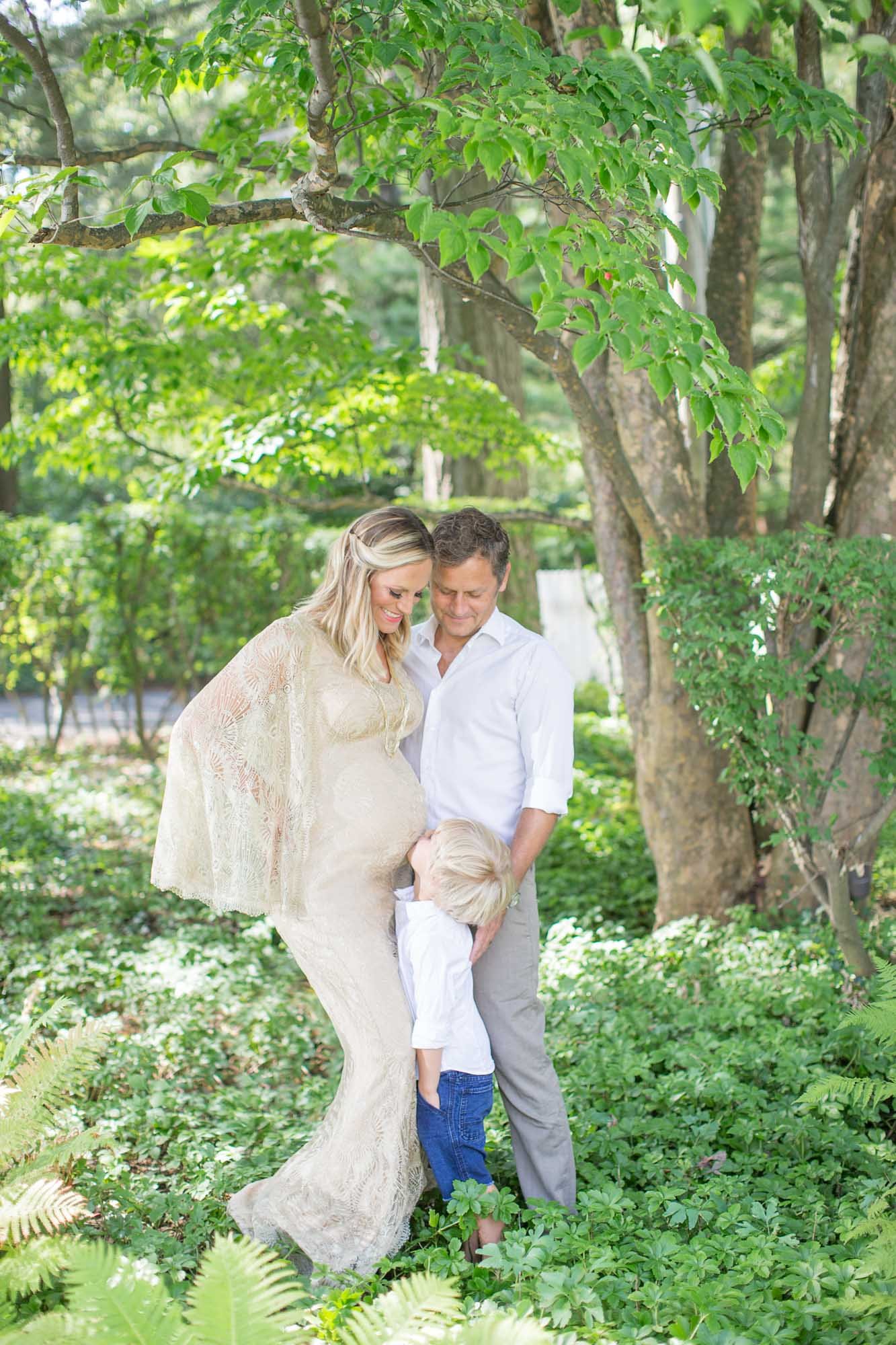 expecting mother with husband and son kissing her pregnant belly outdoors