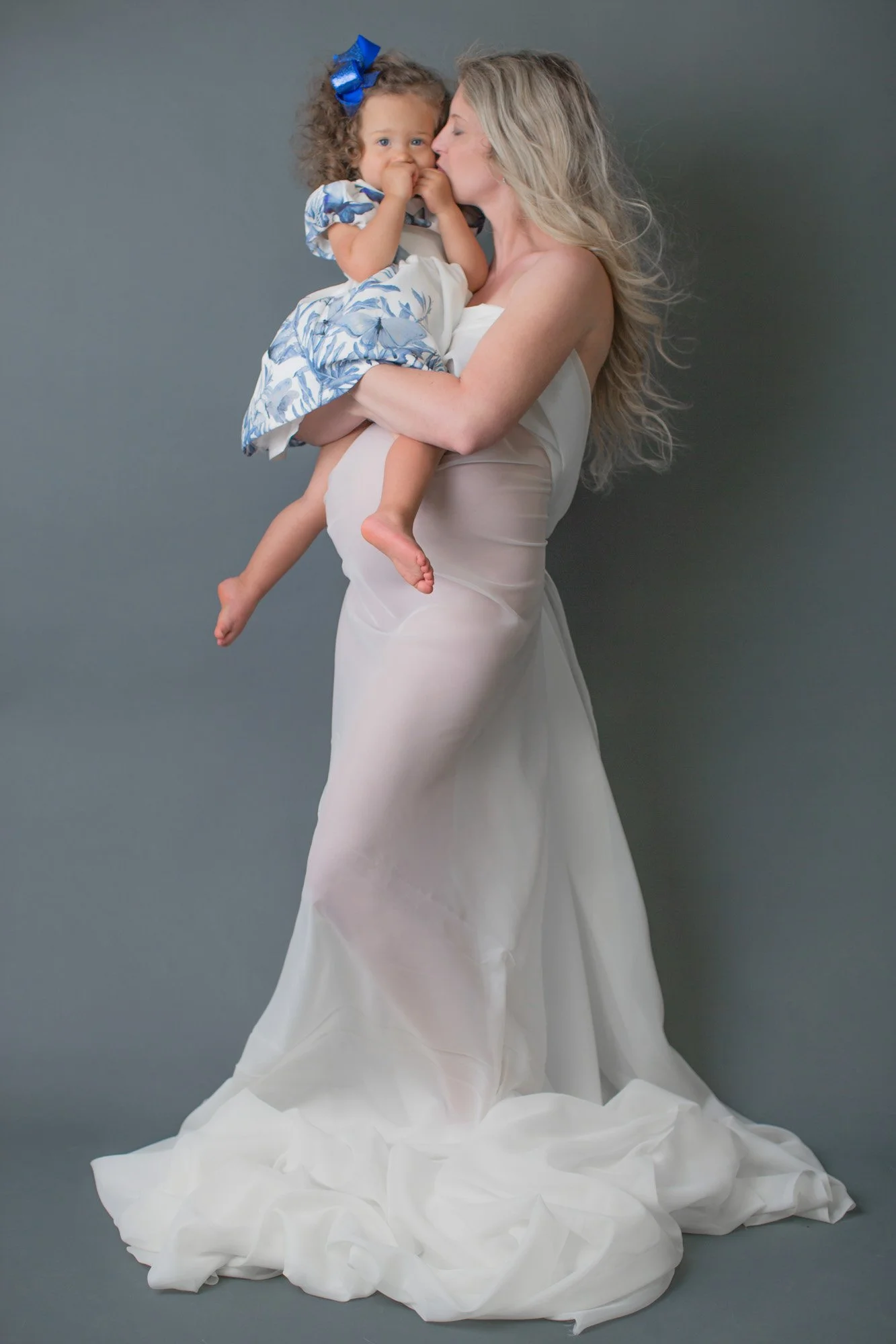 expecting mother studio portrait holding daughter kissing her face with sheer dress
