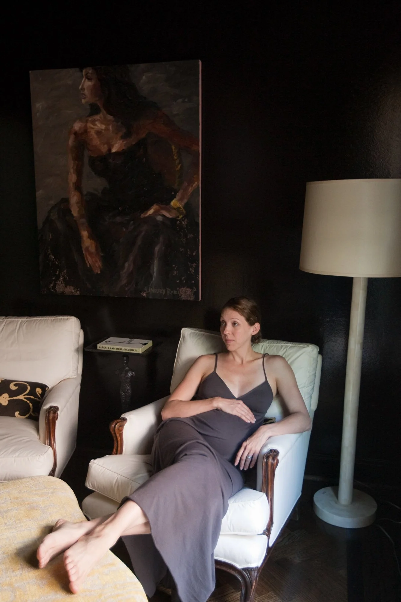 expecting mother sitting inside a window light room with large pinging behind her