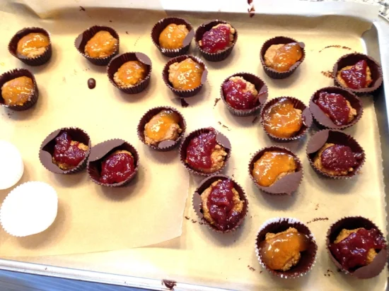 Peanut butter mixture and jam filling added to hardened chocolate cups.