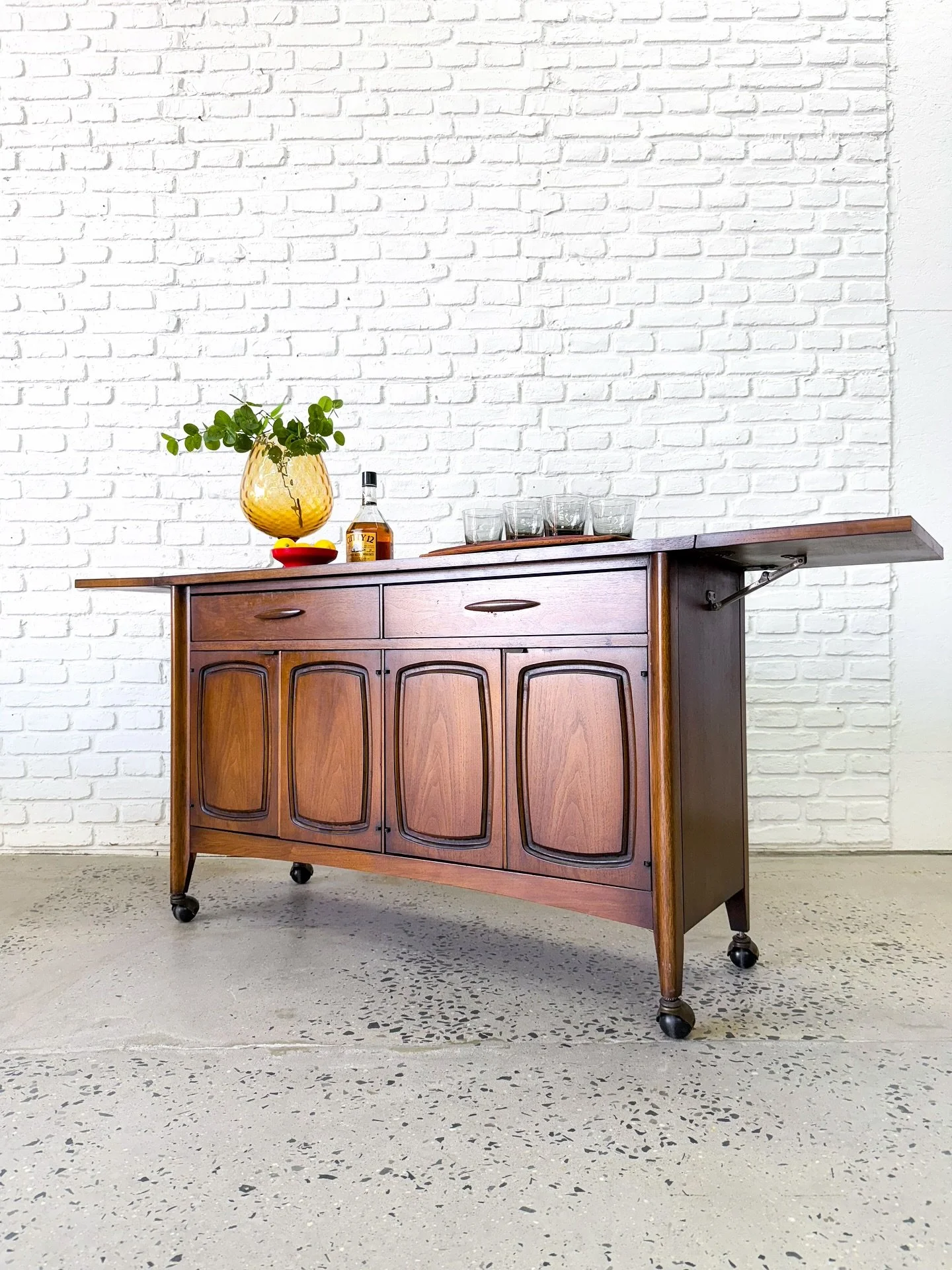 Broyhill Emphasis rolling bar cart with flip up wings that expand the serving surface. Made in the US circa 1960s. Durable black laminate top, with plenty of storage below.
Good original condition with typical signs of vintage use.
48” (70&