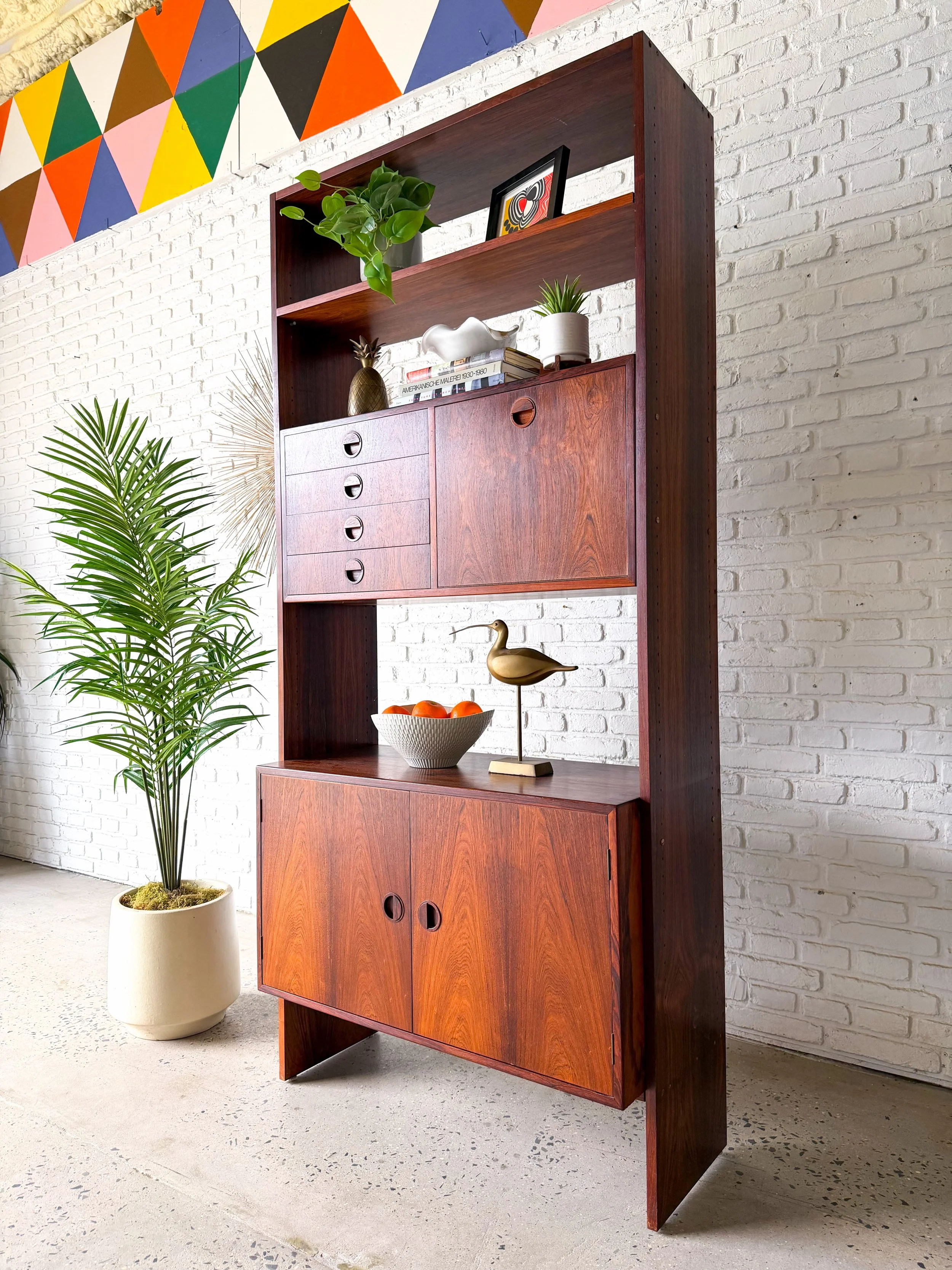 Freestanding rosewood wall unit, made in Denmark. 

Has a drop down bar, 4 small drawers, cabinet storage at the bottom, and open shelving. Just so much storage and display possibilities with a small footprint.

37&rdquo; x 16&rdquo; x 80.25&rdquo; t