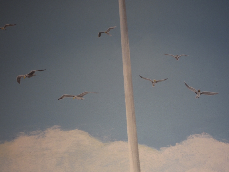 Seagulls circle the mast of the boat riding at anchor.