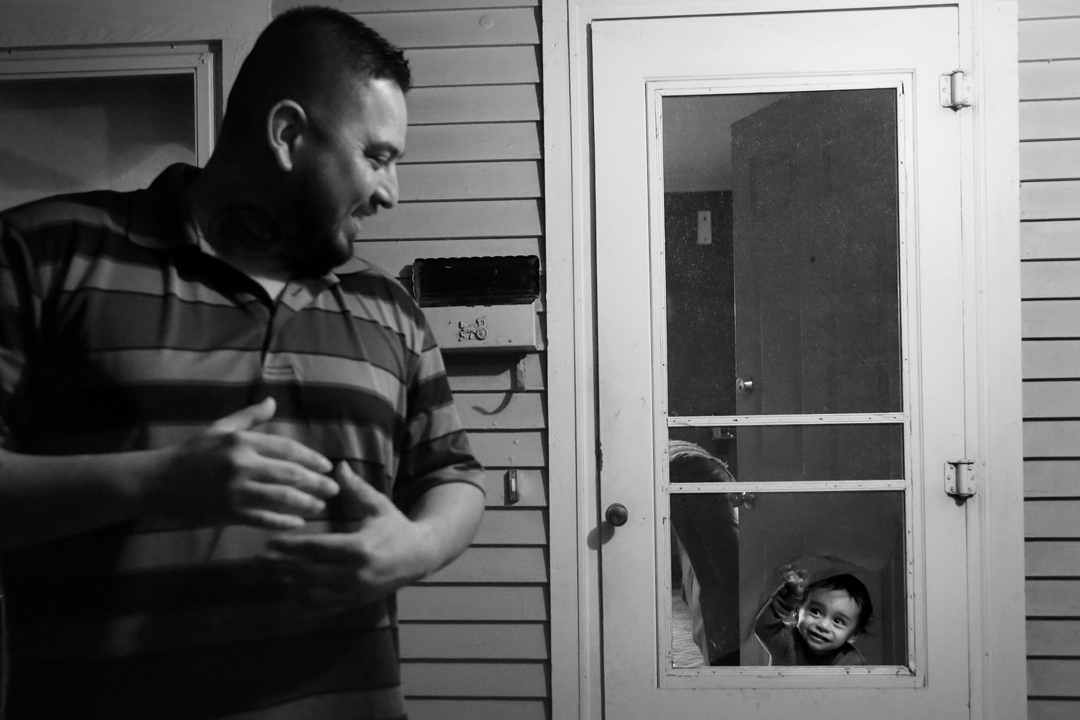  Rojelio Sanchez, left, smiles back as his two-year-old son Rojelio III, peers through a hole in the screen door at the family's home in Napoleon. Since being released from prison after serving 11 years for attempted murder, Rojelio has made it his g