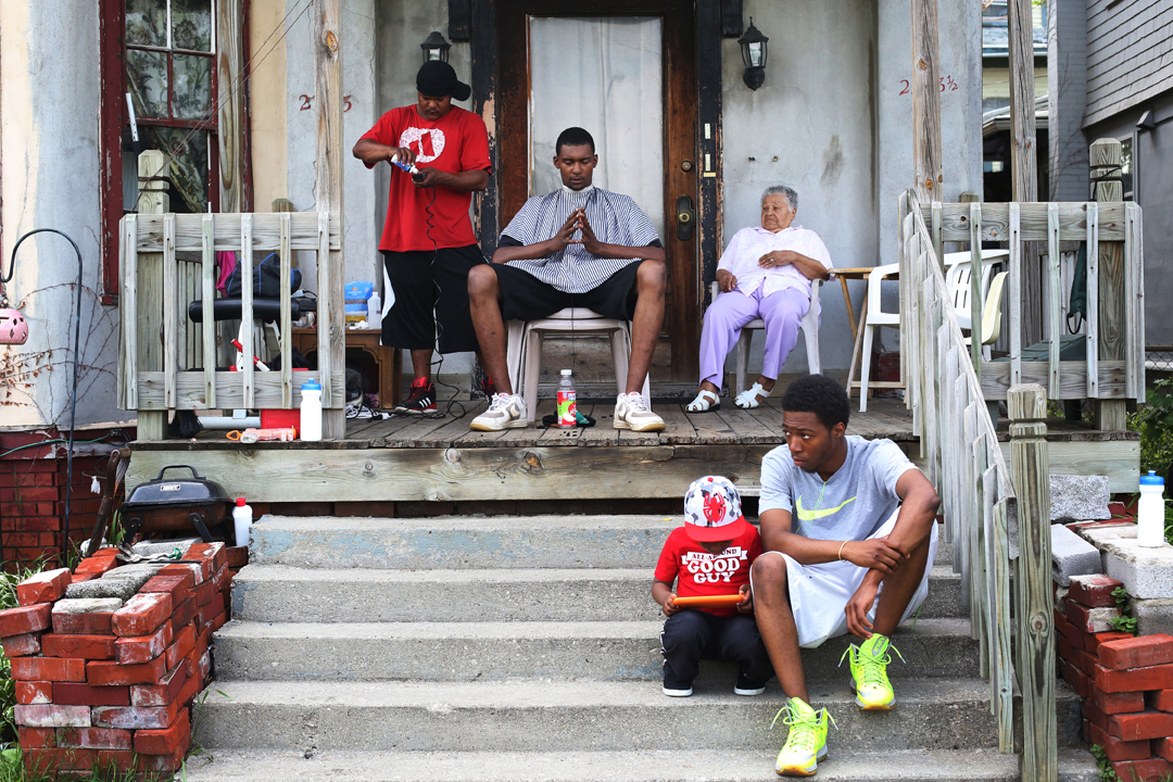  Abayomi Miller, left, gets his clippers ready to cut hair for his neighbor Jason Johnson, center, on Miller's front porch Wednesday, May 21, 2014 in North Toledo. With temperatures climbing into the low 80's, Darren McCadney, right, and his son Zavy