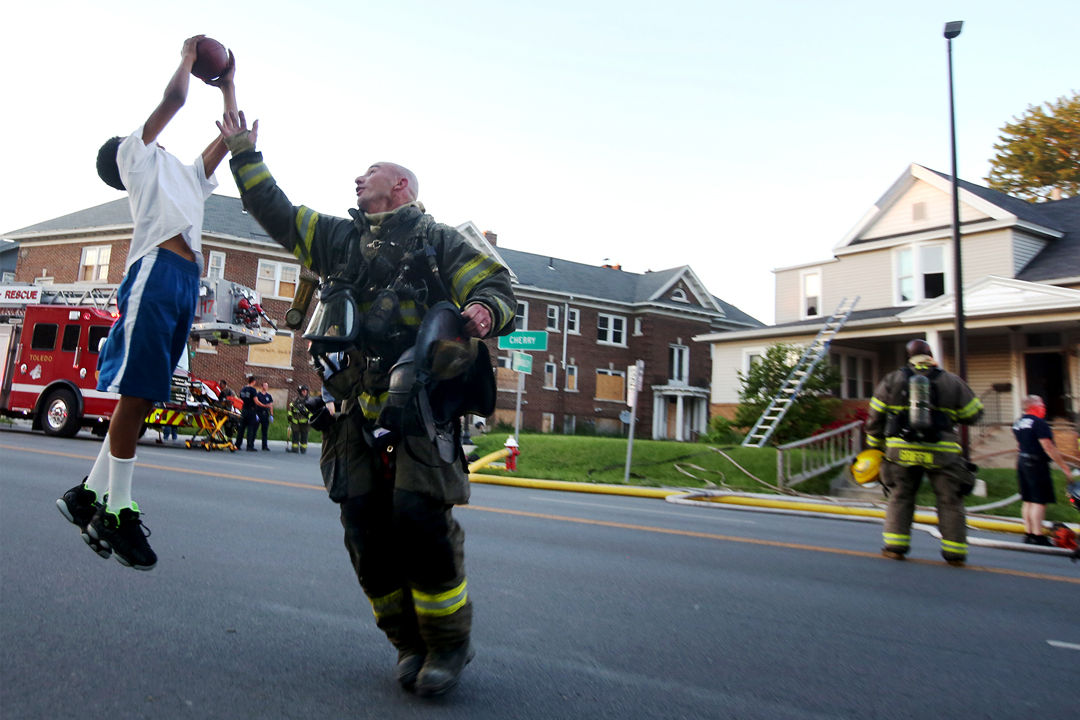  Lt. Pete Traver can't cover Tabari Triplett, 11, as he plays football with some friends from the neighborhood Monday, June 5, 2017, after Toledo firefighters had extinguished a blaze at a house on Cherry Street in Toledo. Battalion Chief Brent Wettl