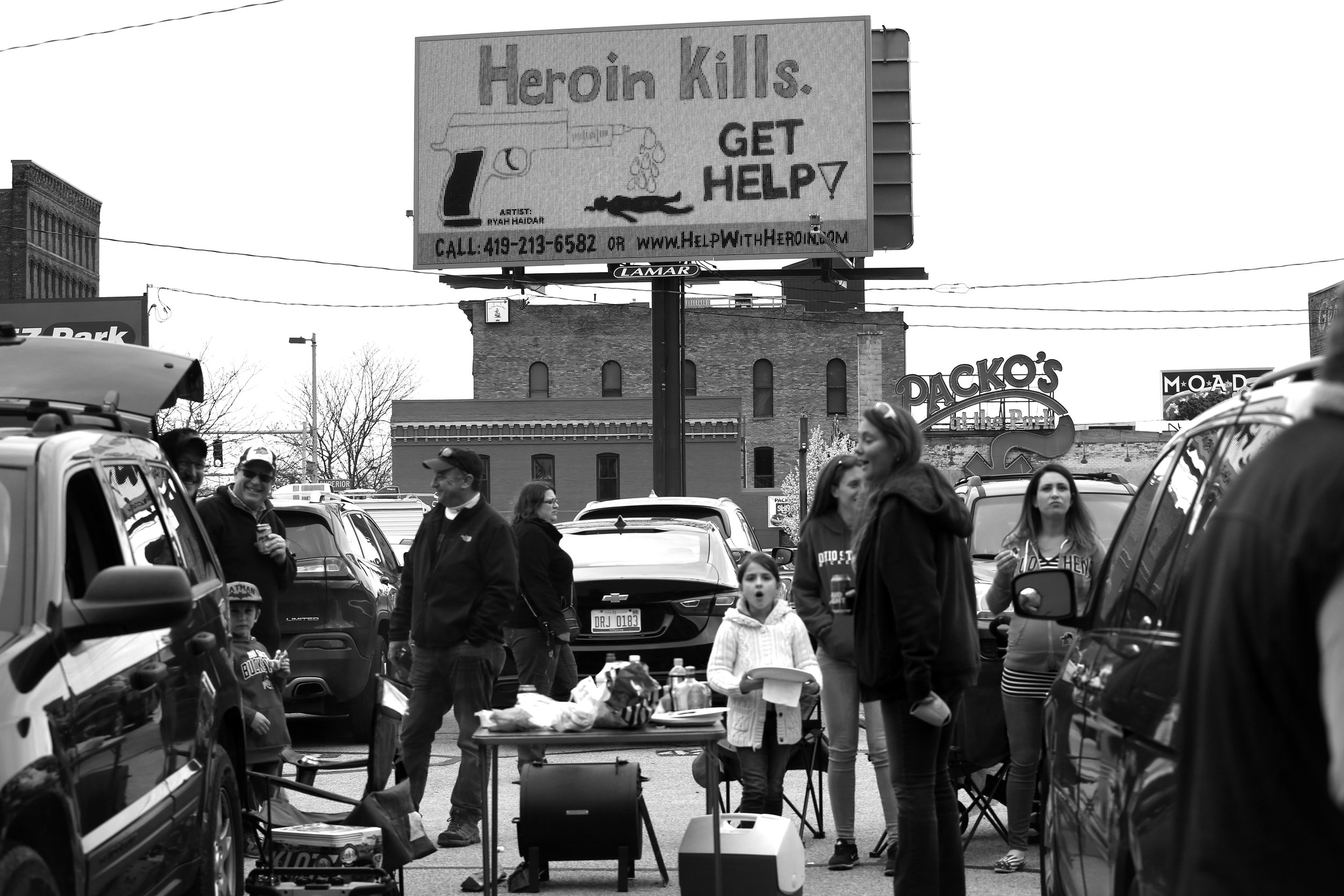  A billboard imploring addicts to seek treatment overshadows tailgaters having a cook-out at Fifth Third Field in downtown Toledo, Ohio, for the Opening Day of the Toledo Mud Hens baseball season on April 13, 2017. The crisis of opioid addiction impa