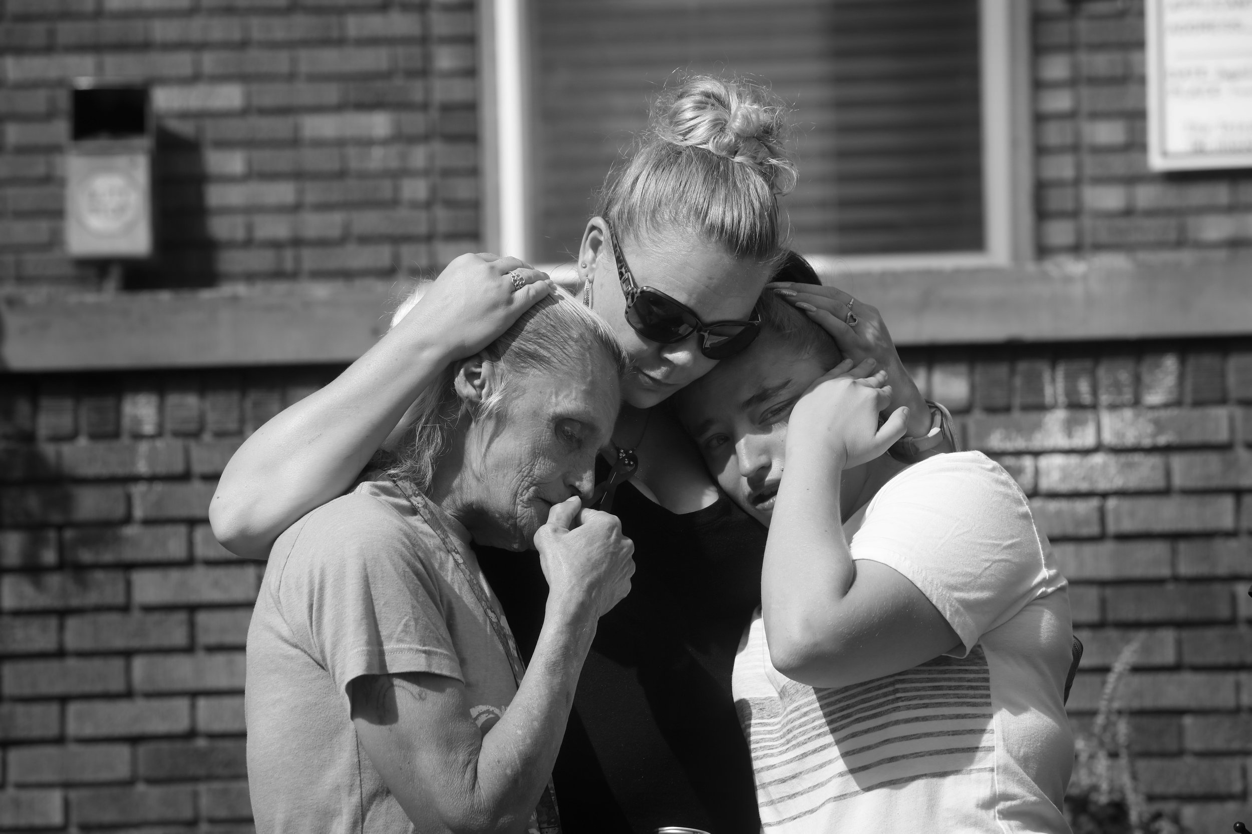  Mother, left, and daughter, right, are embraced by a friend as they remember a family member, who died of complications from opioid addiction, during a remembrance event at the Northwest Ohio Syringe Services, a harm reduction program that works wit