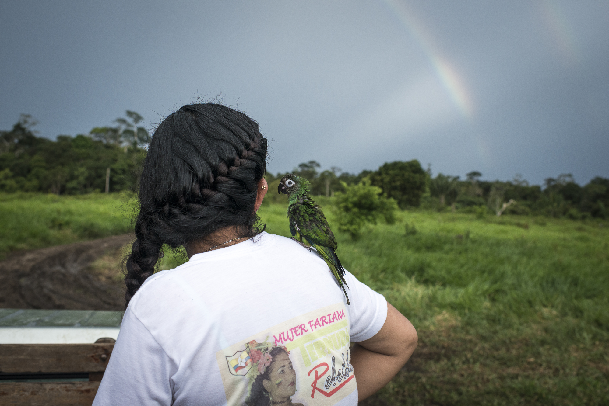 June 2016, South Caquetá. Fernanda and Paquita, her baby parrot, are looking at a double rainbow at the end of a day. On her t-shirt is writing “Mujer Fariana”, woman of the FARC culture.Criticized by the past for the lack of space given to female and LGBTI rights, the FARC guerrilla promoted in contrast a gender dimension into the first peace deal signed on September 26, 2016. But on October 2, 50,22% of the referendum voters rejected the agreement. A new peace deal has been negotiated and signed on November 24, with almost all the gender references removed according to the evangelical churches request, which were among the most powerful No promoters.