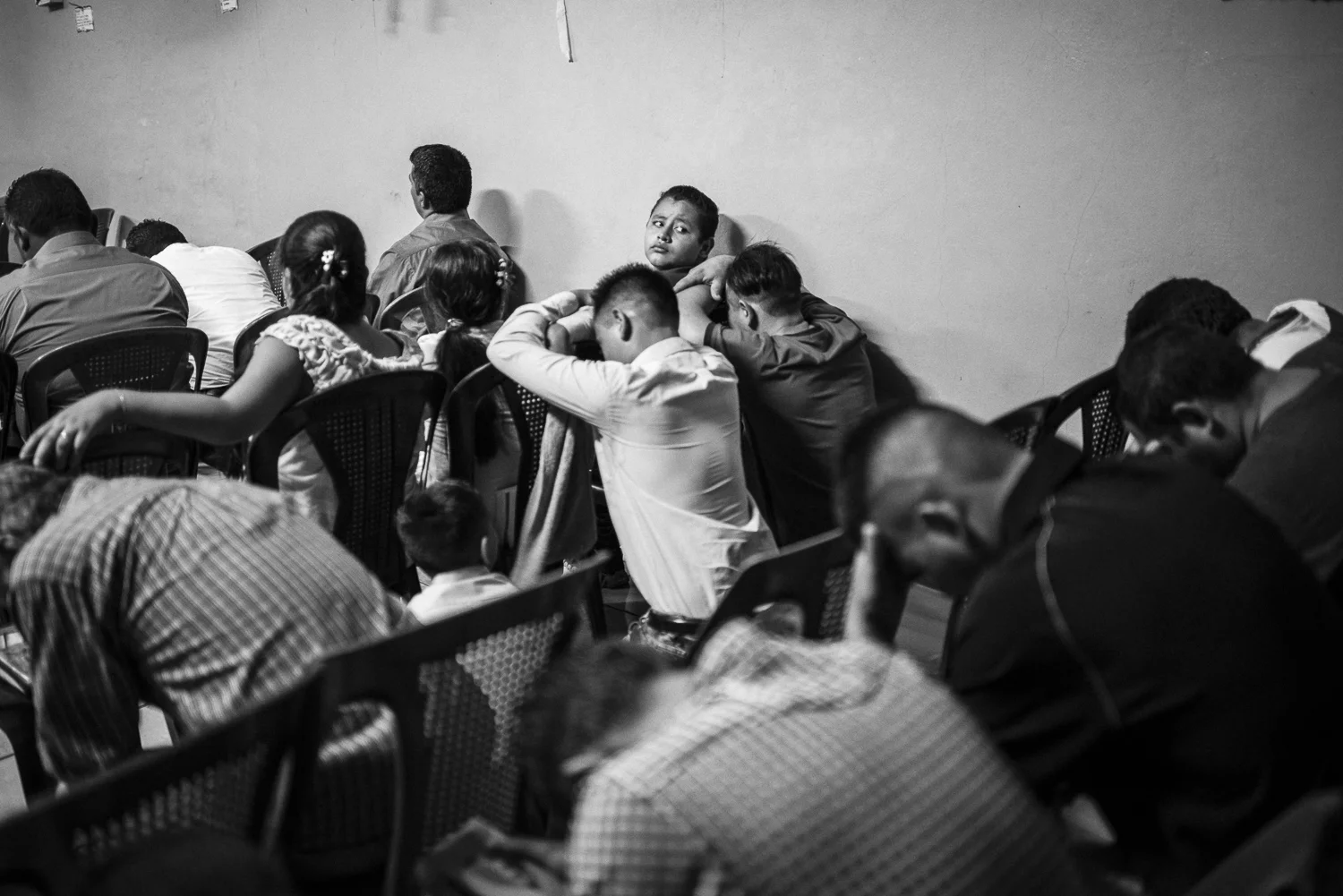 A young boy is looking behind him at the time of a evangelical worship, a Sunday morning in a colony of Aguilares (El Salvador, October 8, 2017). A group of former gang members converted to evangelism come here to convince gang members from the Barrio 18 to convert. They founded a Church “The New Creation” that the only purpose is to receive former gang members when they are released, or to convert the gang members. According to David Munguía Payés, minister of Defense, there is 60,000 active gang members in El Salvador. The gangs exercise strong pressures on the young people to recruit them. And most of the public forces think a gang member will stay a criminal for life. And now, the stigmatization is spreading on the young people of the popular districts, easily assimilated to the gang for living on an area under control. Credit: Nadège Mazars / Hans Lucas studio