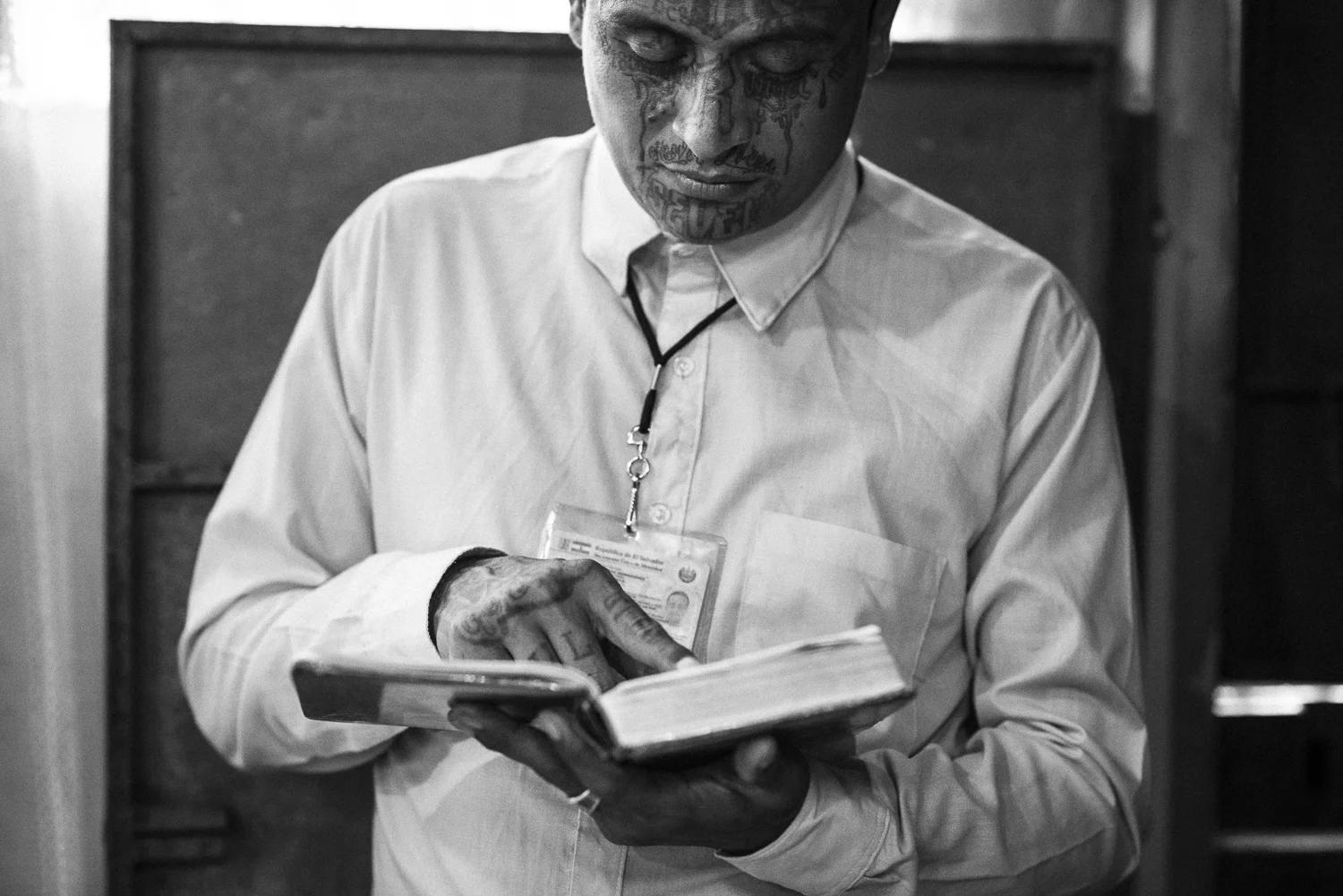 Roberto is reading a bible, a Sunday at the time of the worship at Eber Ezer Church. The tattoos cover his face. They name or allude to his former gang, 18-R, a split of the initial gang 18. (San Salvador, July 02, 2017) The chief gangs let only two possibilities to let formally the gang: or by dying, or by dedicating his life to God. There is no real rehabilitation policy from the Salvadorian State that could give to the former gang members other alternative. Credit: Nadège Mazars / Hans Lucas studio
