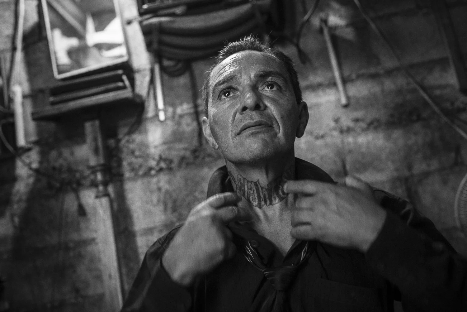 Edwin unbuttons his shirt. His opened collar reveals his tattoo with the name of his former gang, Eighteen, usually hidden under his tie strictly adjusted. Edwin is a former gang member. He left the gang in 2010 after an “encounter with God under the shadow of terror”. He is a migrant’s child. He came in United States in his childhood and entered in the “18” gang there. After several years in jail, he was deported and participated with others deported to the expansion of the gang in El Salvador. (San Salvador, El Salvador, October 10, 2017) To see his tattoo, I ask Edwin to show me what are the movements he does everyday to attach his tie. I was impressed how the tattoo want to remerge while he lifts up the head to pray. Like if there was a kind of symbolic fight between the tie and his devil inside. Credit: Nadège Mazars / Hans Lucas studio