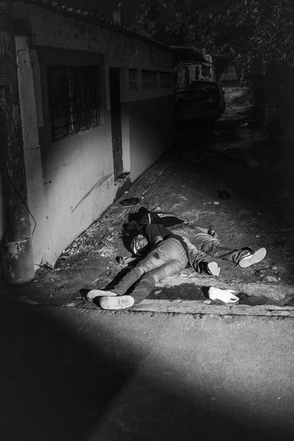 A policeman lights the bodies of two young men found on a dark alley of Santa Isabel colony, territory of the MS-13 gang. According to the police investigation, the two men were members of the MS-13 and were executed to no comply the internal rules. (Soyapango, El Salvador, July 8, 2017) The homicide rate in El Salvador signi cantly reduced, coming down to 60 per 100.000 in 2017 instead of 81,2 in 2016 (Insight Crime). But El Salvador stays the second most homicidal country in Latin America. Credit: Nadège Mazars / Hans Lucas studio
