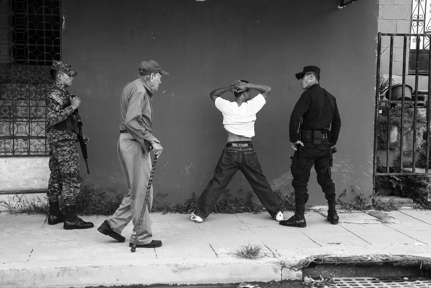 A police patrol assisted by militaries is checking the documents of a “retired” gang member, now evangelist. An old man came to see if everything goes right (22 de Abril colony, Soyapango, El Salvador, July 8, 2017) Credit: Nadège Mazars / Hans Lucas studio