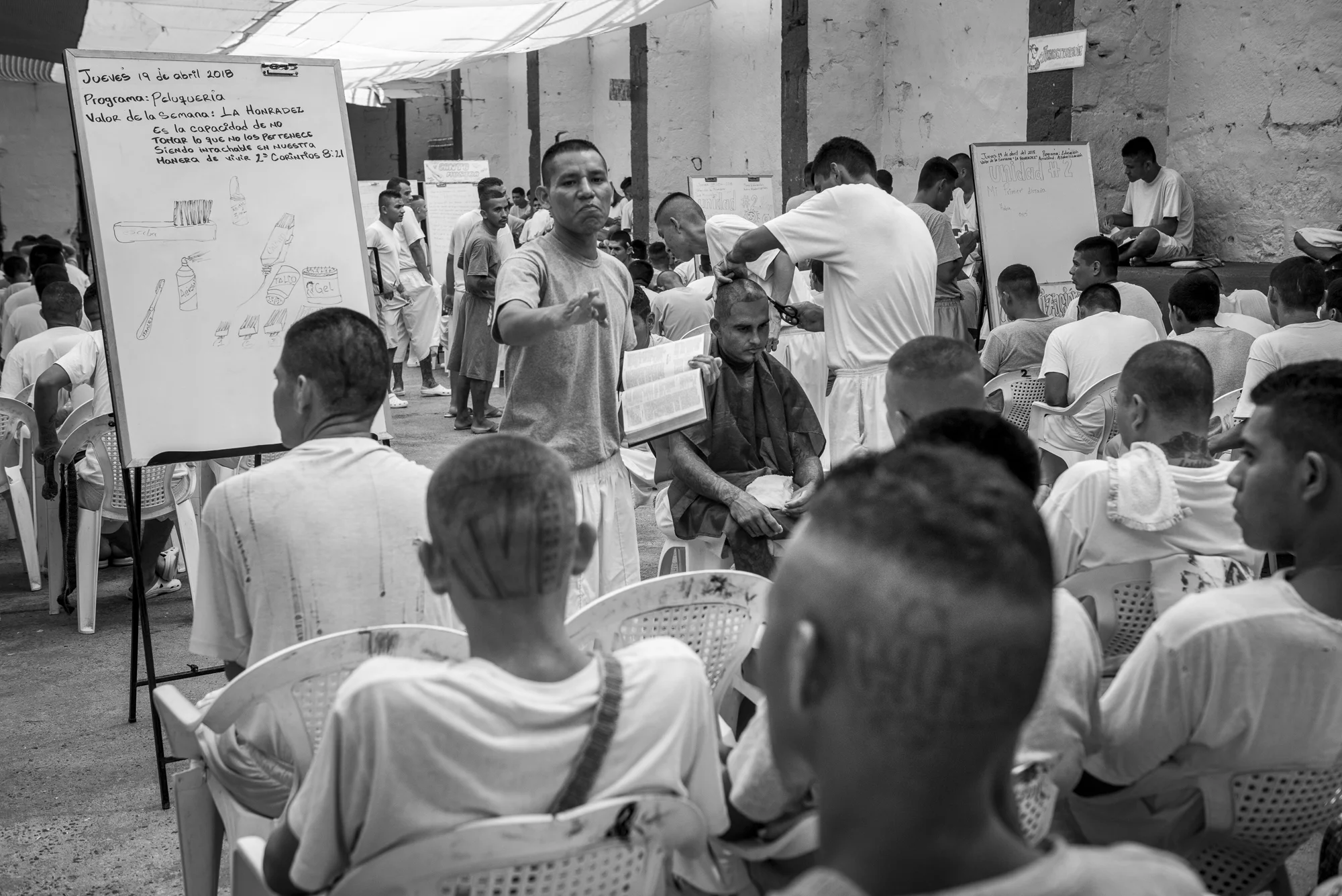 A group of prisoners is listening the class an inmate is giving about haircut. A verse of the Bible is recalled on the whiteboard. Inside every yard, the inmates are participating to a class where they can learn a practical training (about bakery, serigraphy, carpentry, etc.), a religious education or an alphabetization class. Since almost two years, the government of El Salvador started a program of reinsertion inside the prisons, named “Yo Cambio”, “I Change”. In La Gotera jail, the director mixed the program with religious instructions.