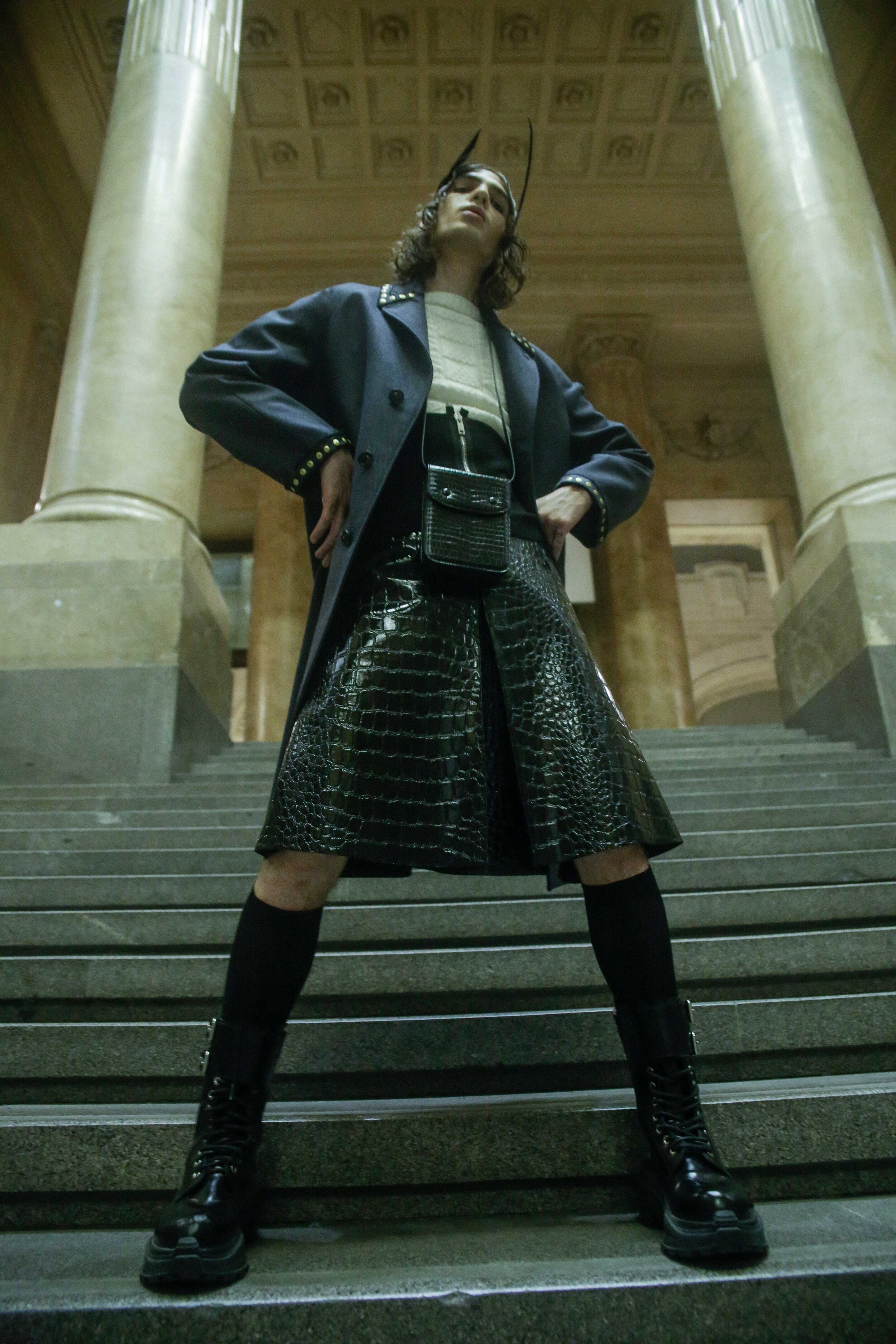 MAISON MARGIELA coat, sweater, skirt, boots, and bag, GIVENCHY corset, and FLAVIA CAVALCANTI feather headpiece.