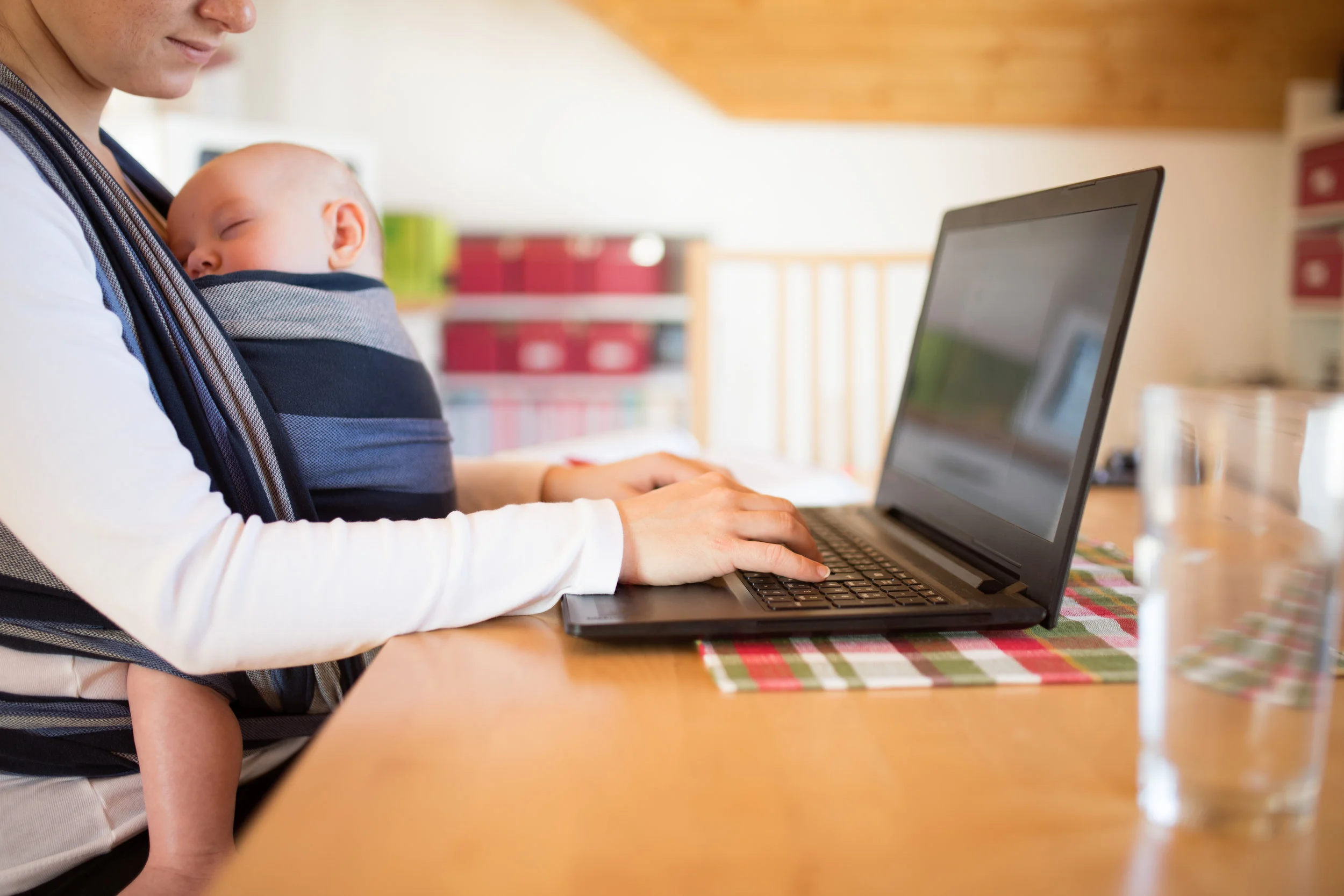 graphicstock-unrecognizable-young-mother-with-her-newborn-baby-son-sleeping-in-sling-at-home-sitting-at-the-table-writing-on-notebook-keyboard_H_-TALKIMb.jpg